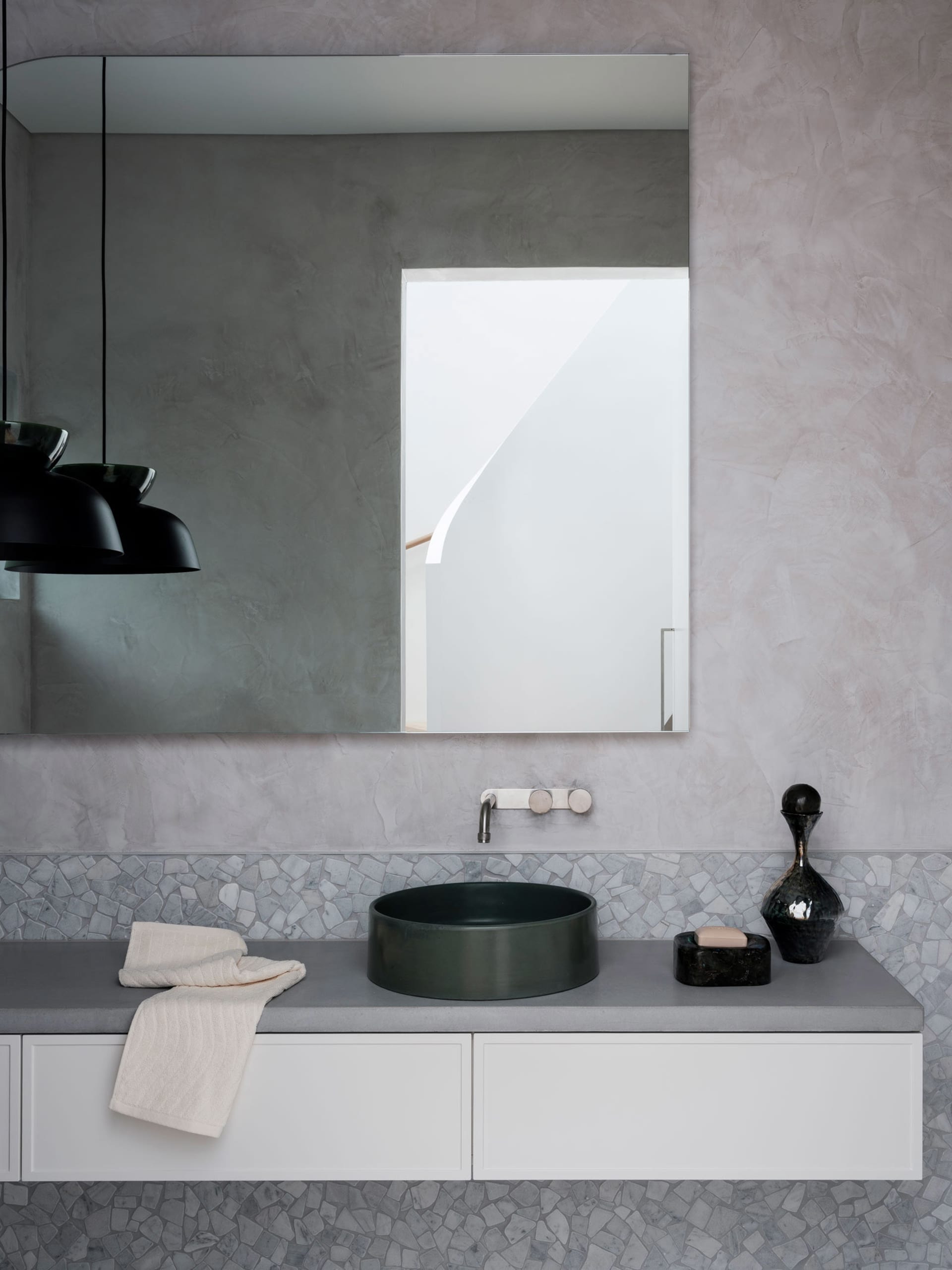 A minimalist modern bathroom featuring a sleek black sink, white cabinets, and a large rectangular mirror with concrete textu