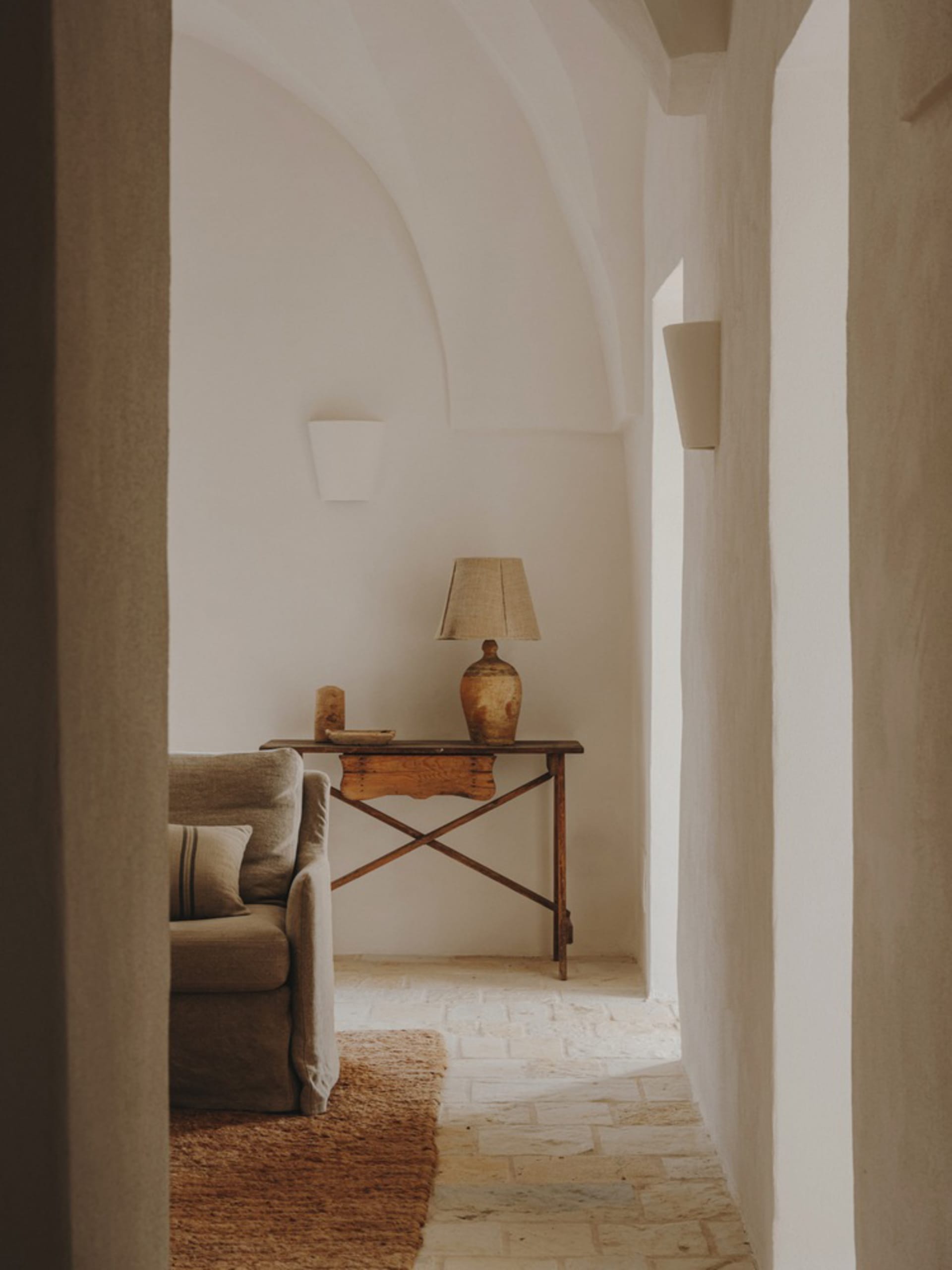 A minimalist living room with a wooden table, beige couch, and beige lampshade.