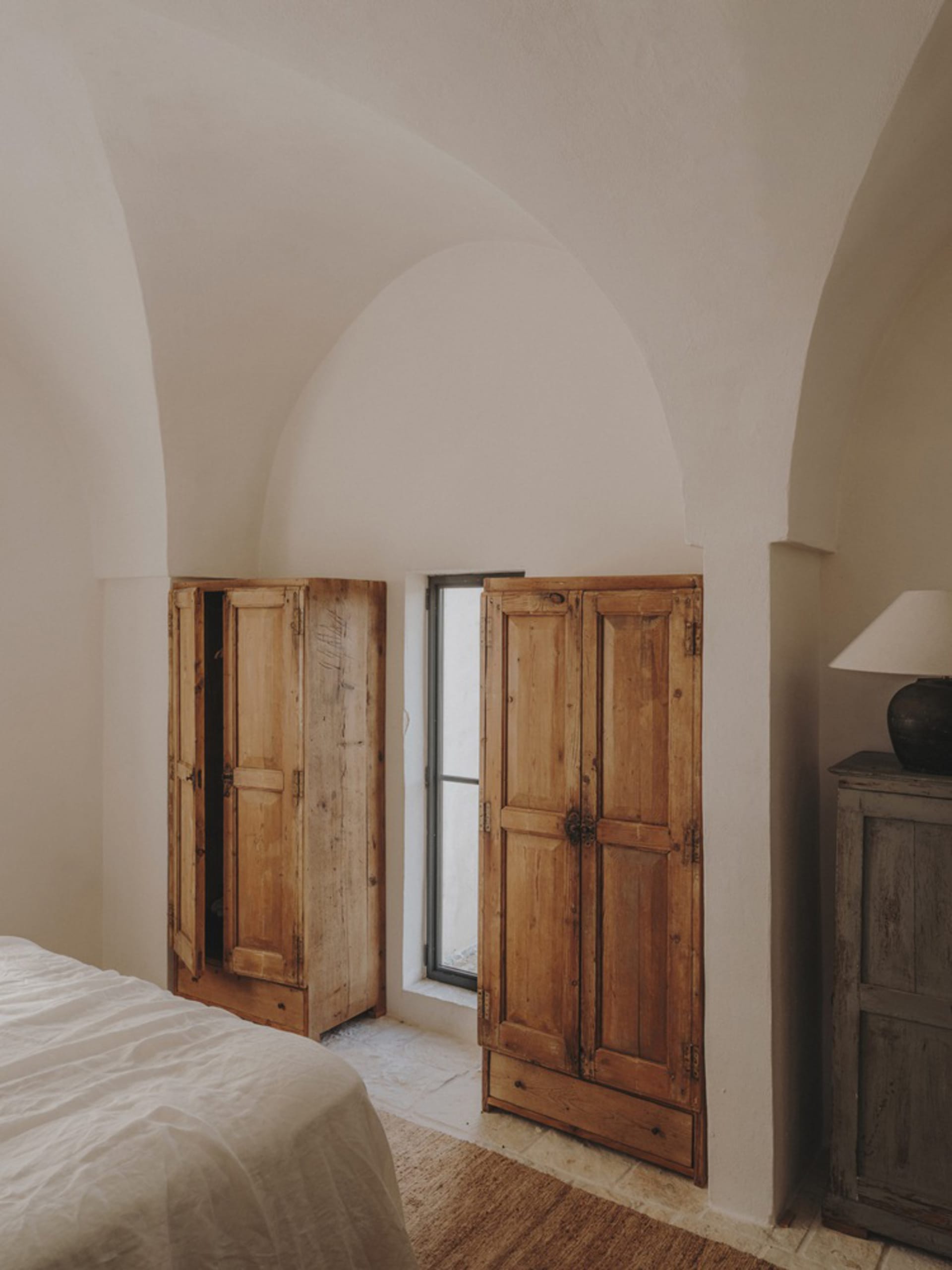 簡約臥室內擺放木質家具，搭配白色床品，以及一扇可眺望戶外景色的窗戶。
