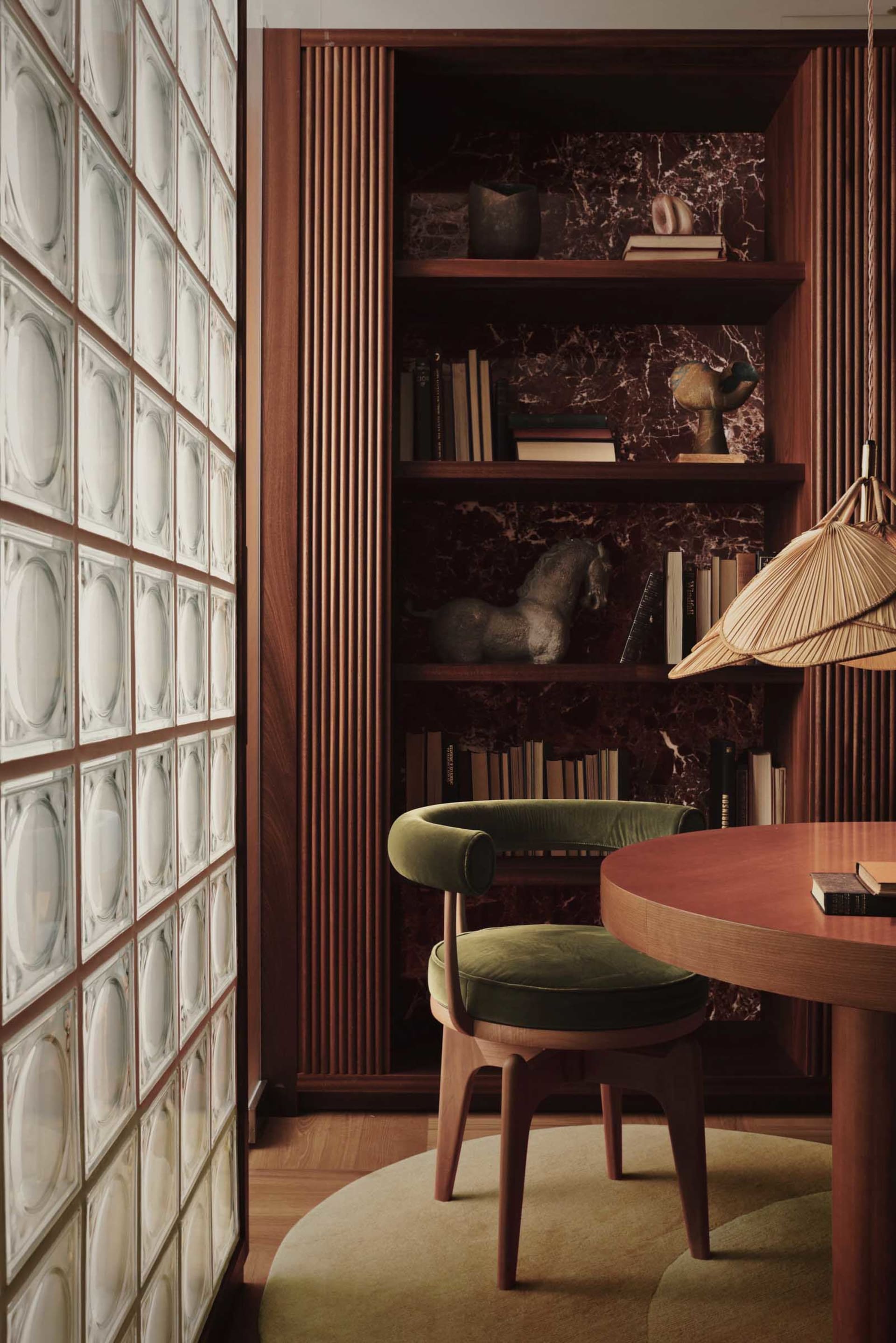 A well-designed home office featuring wooden shelving and a round wooden table with a green cushioned chair.