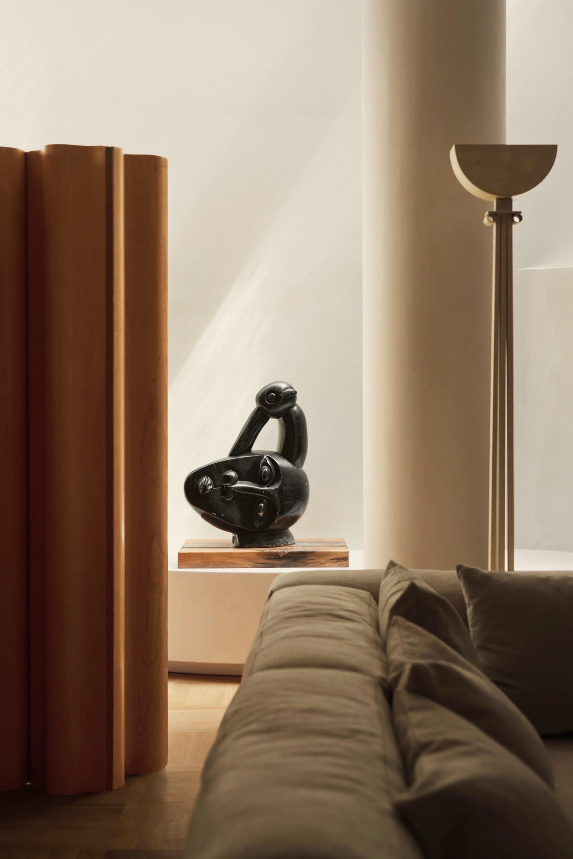 A modern living room with a wooden sofa and a black bird sculpture on a shelf.