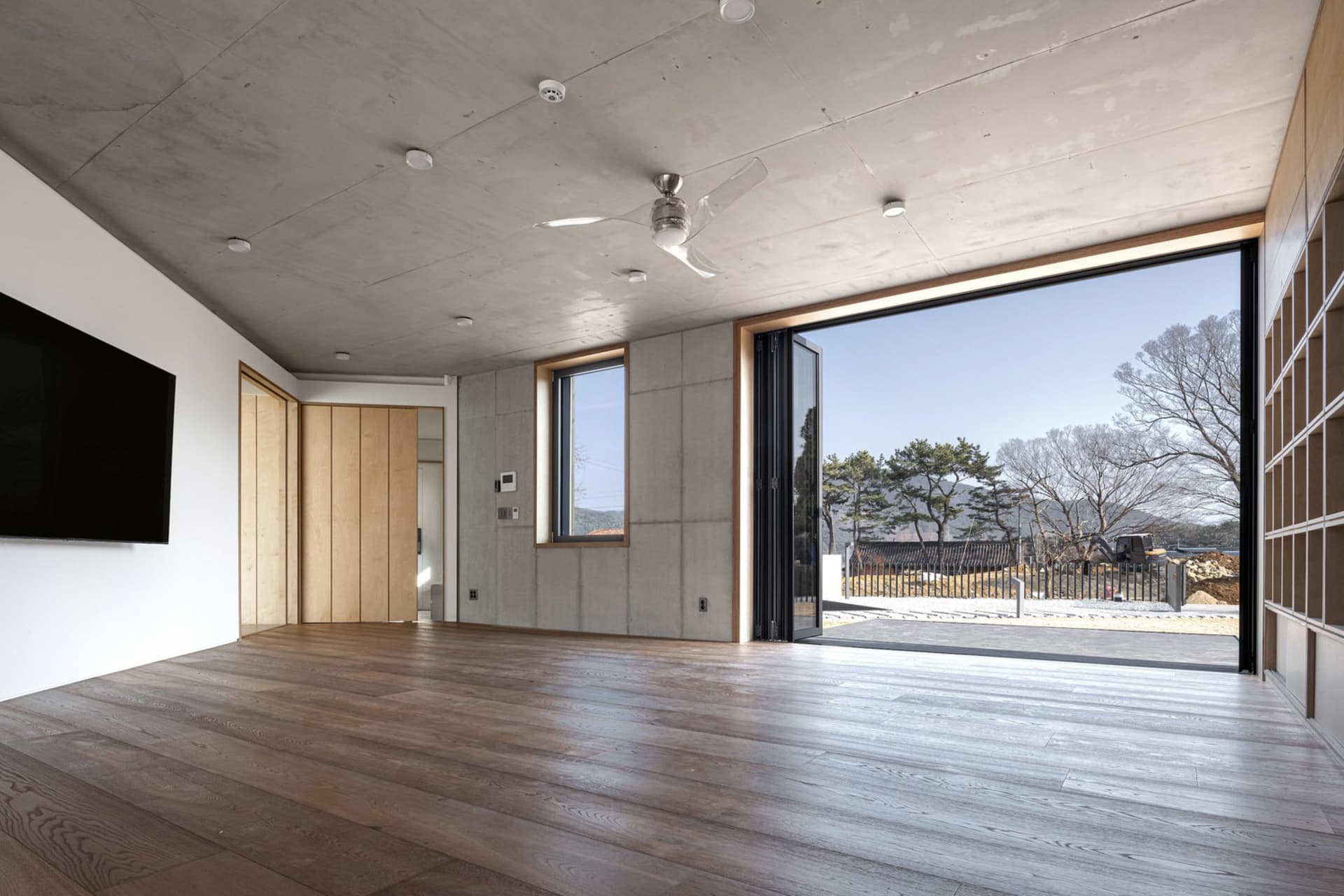 A modern minimalist living room with concrete walls, large windows, and a wooden floor.