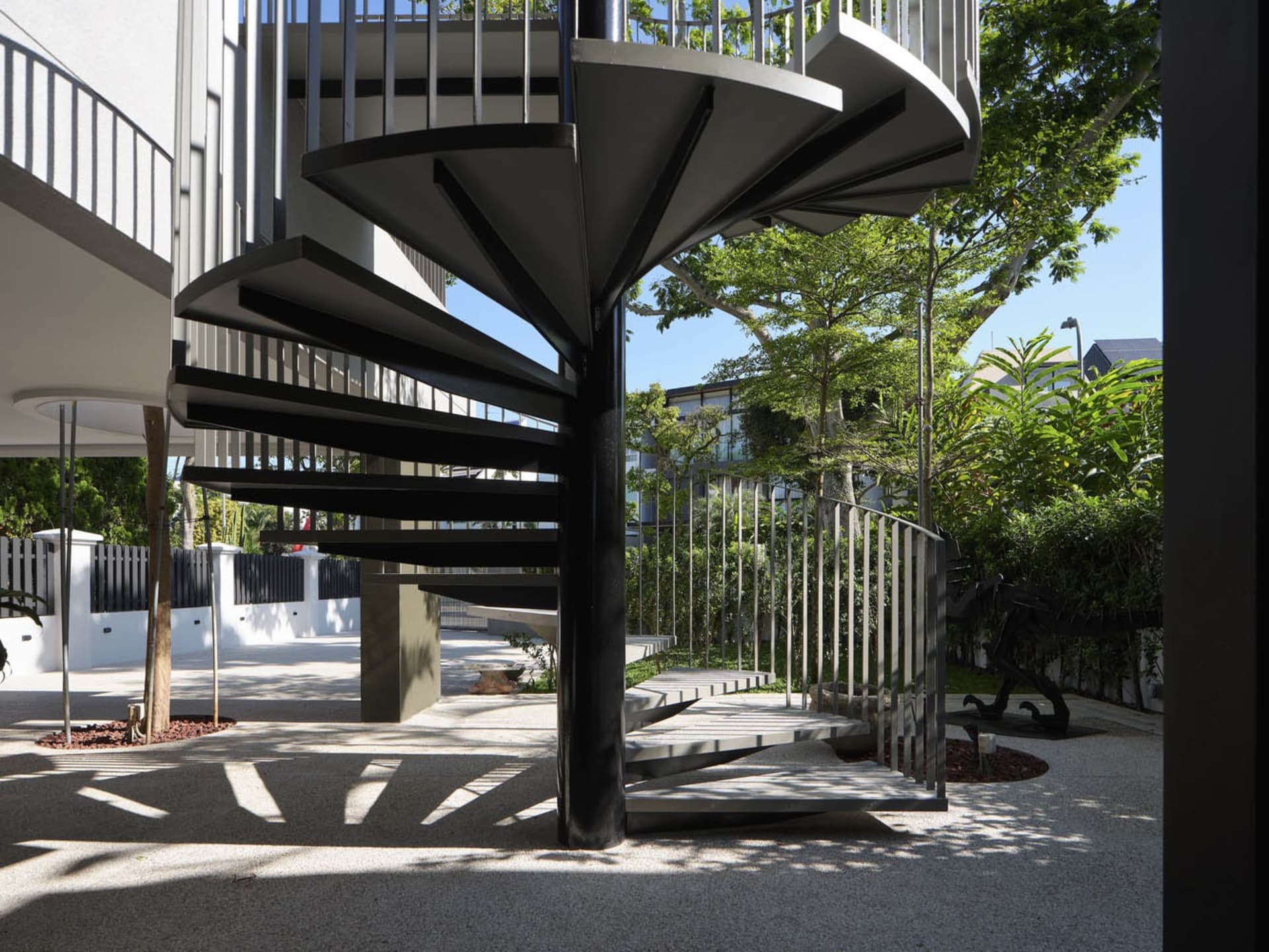 Outdoor spiral staircase with black metal railings and steps, framed by greenery and trees.