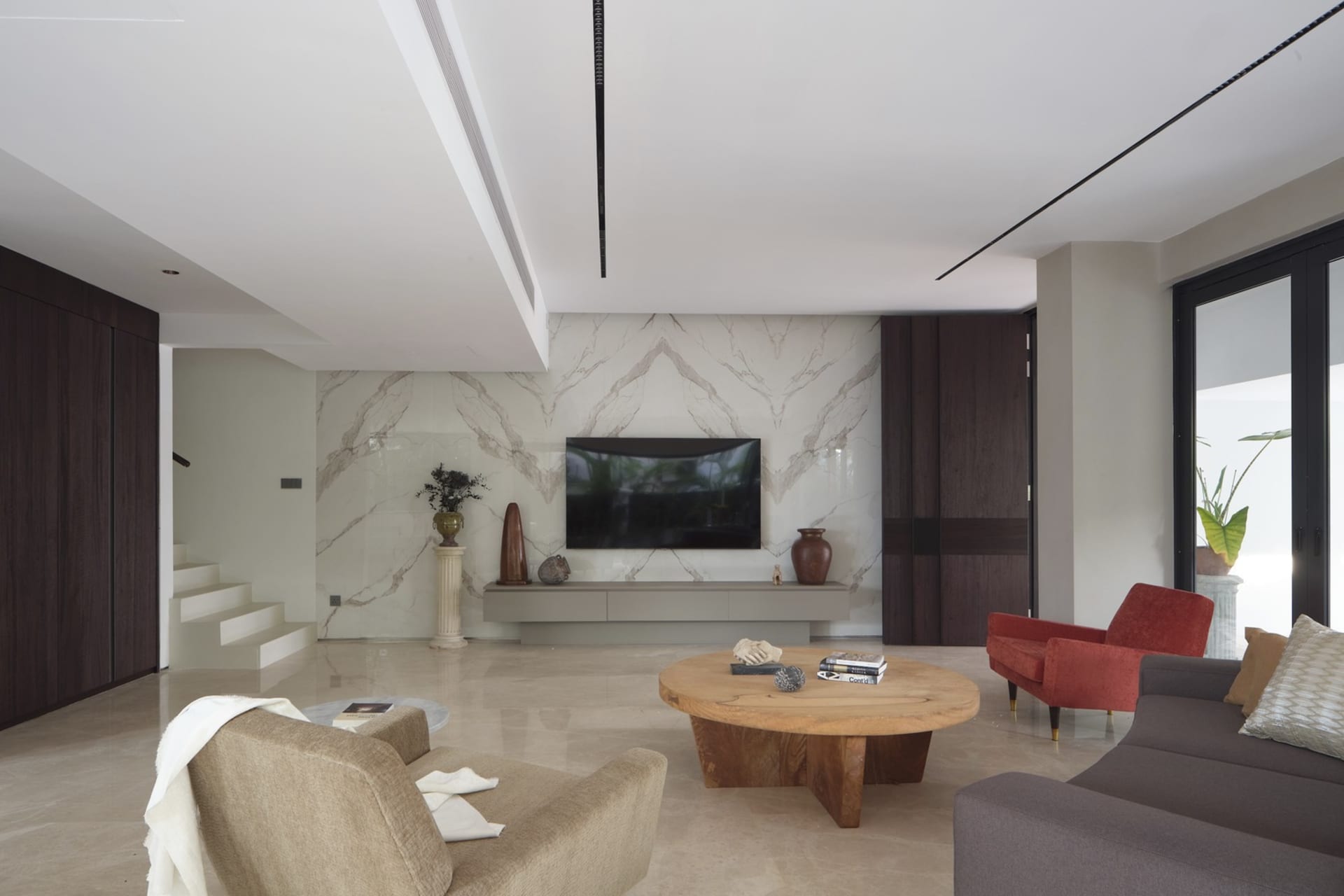A modern living room with a marble accent wall, a wooden coffee table, and a television on a white cabinet.
