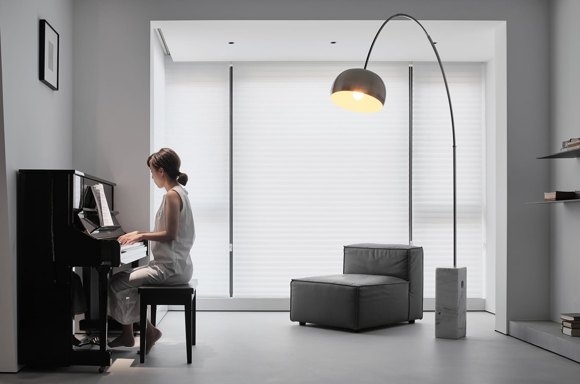 A minimalist living room with white walls, a black piano, and a gray couch.