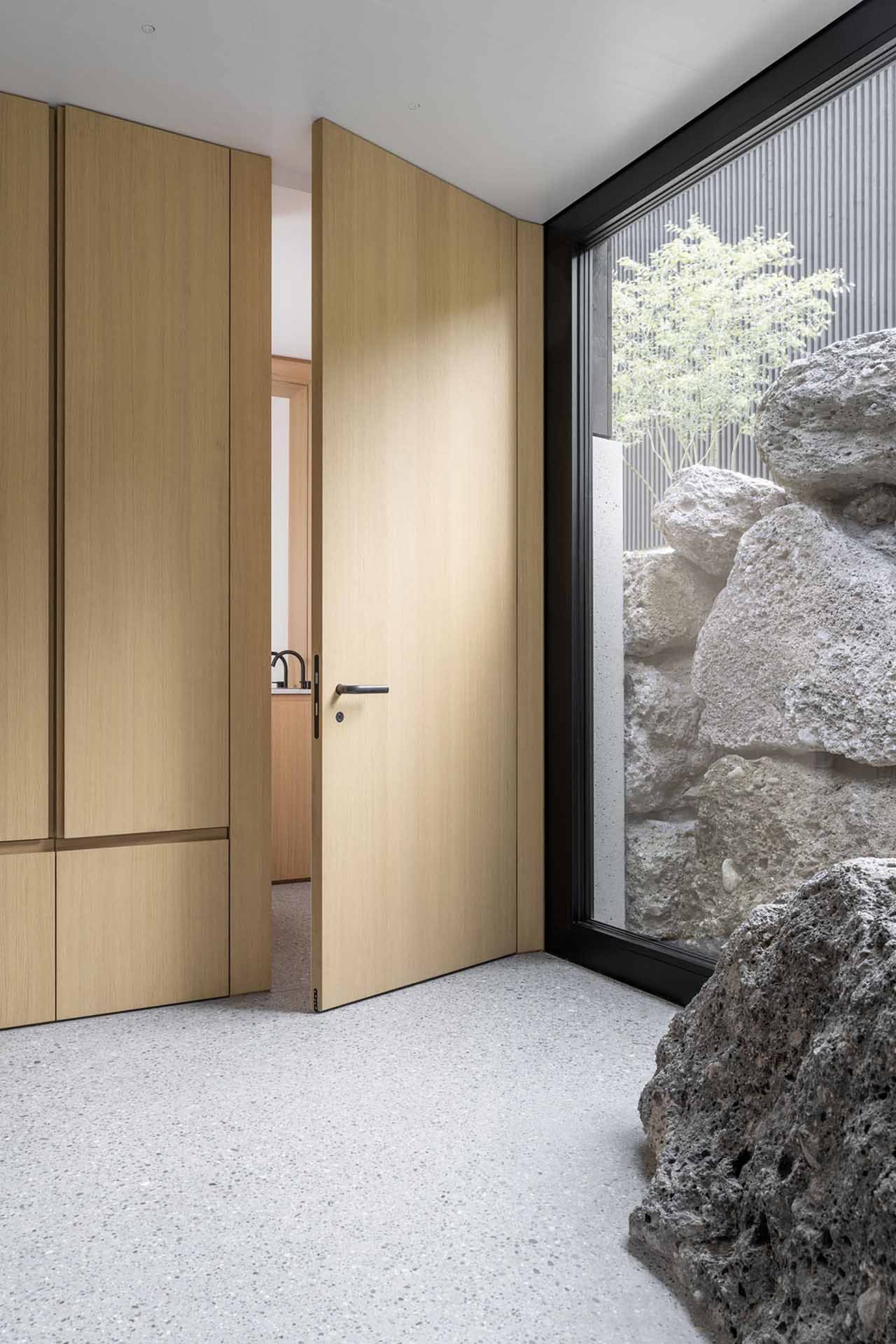 Modern entrance with wooden door, concrete floor, and rock wall