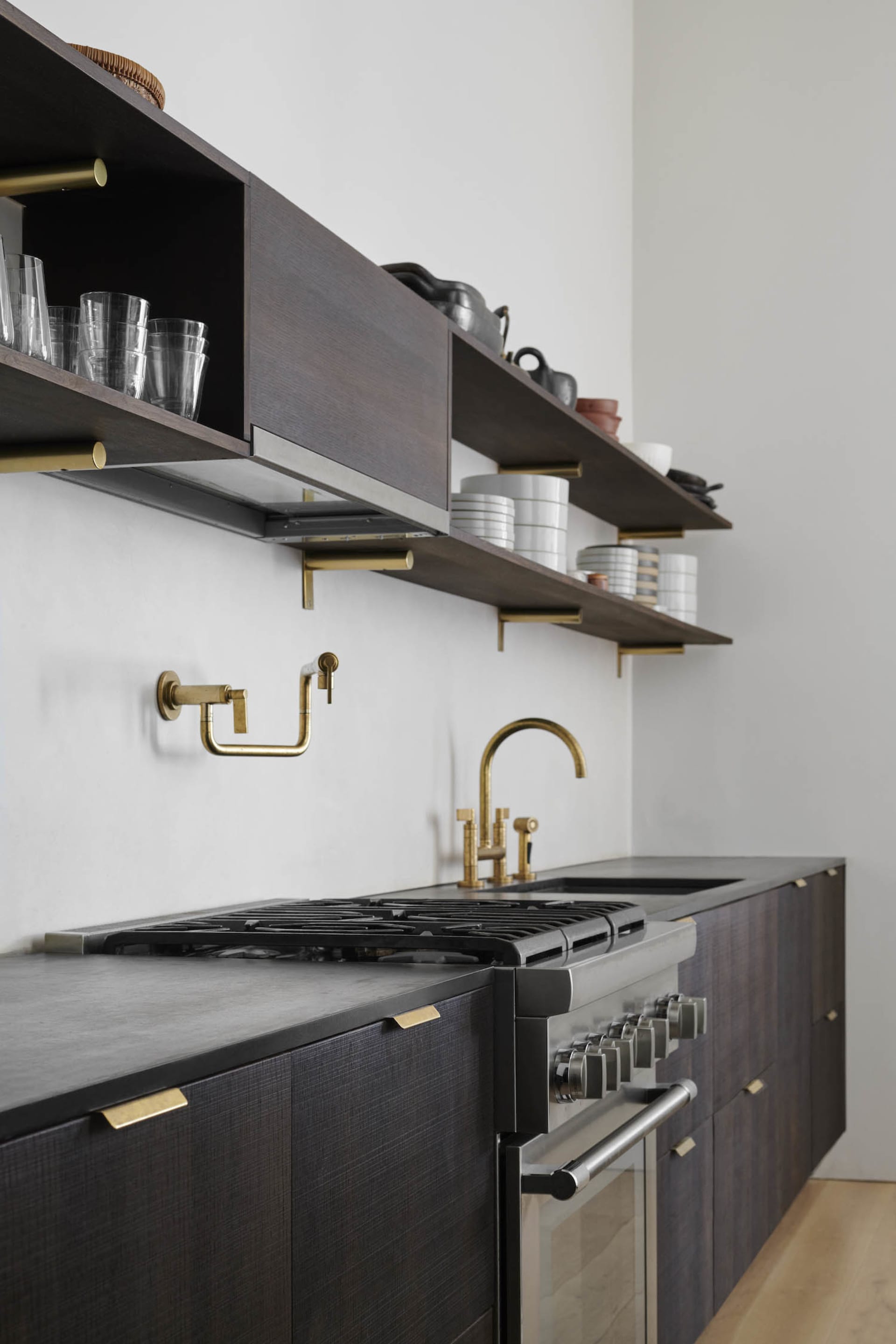 A modern industrial kitchen with dark wood cabinets, brass accents, concrete countertops, and glassware.