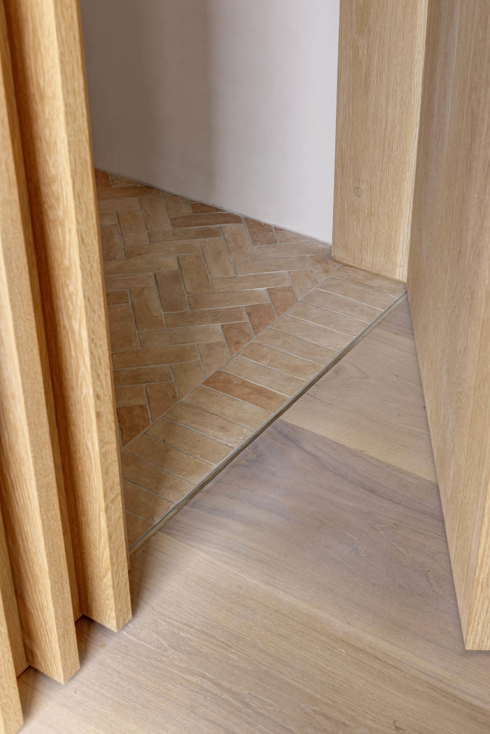 A wooden floor meets ceramic tiles in a transitional corner, showcasing a seamless blend of natural and modern materials.