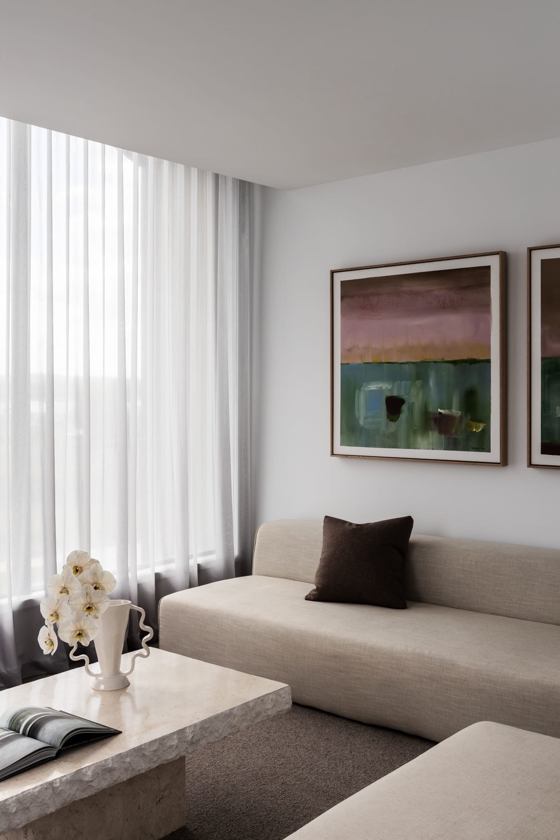 Modern minimalist living room with neutral tones, upholstered furniture, and abstract artwork.
