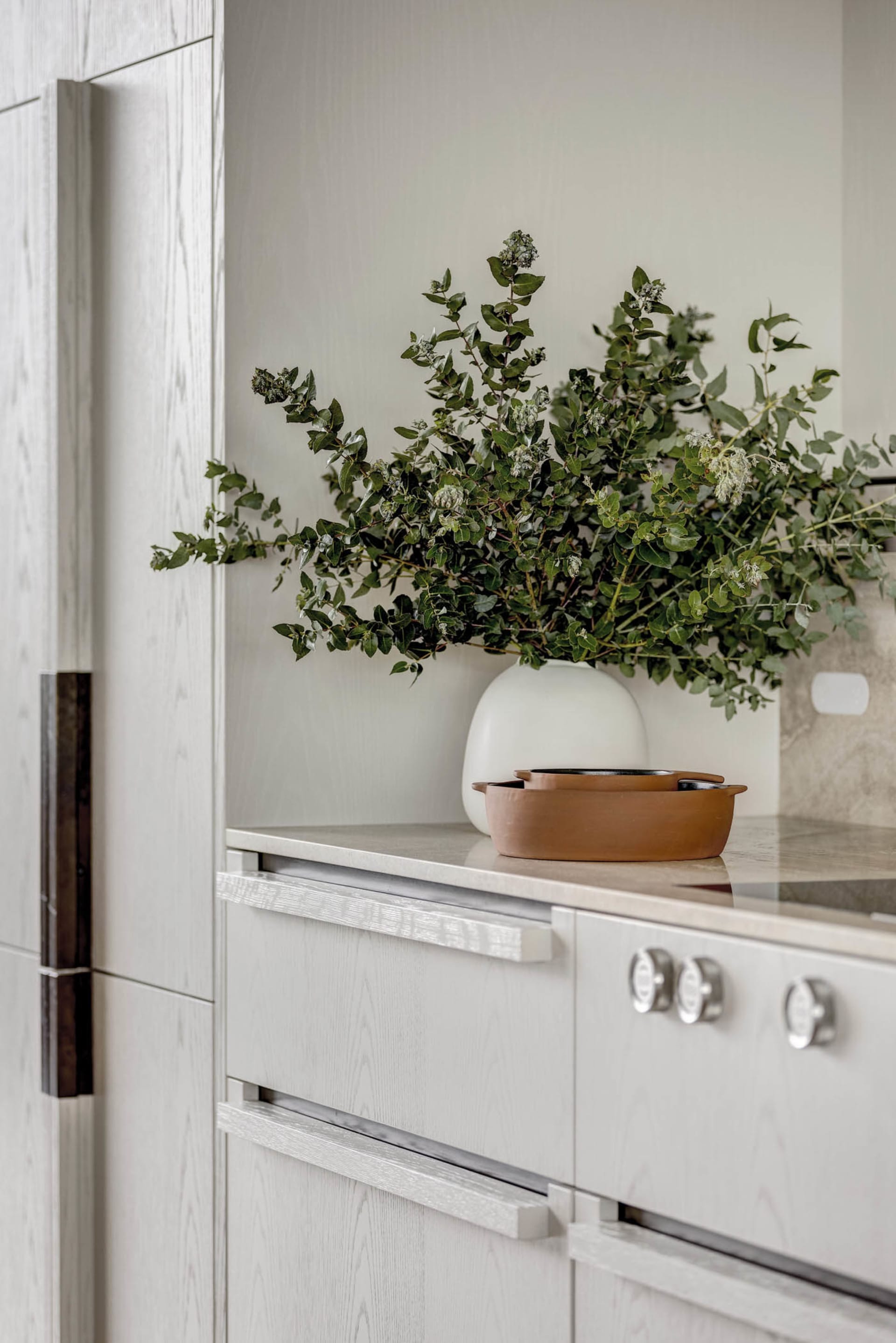 Modern minimalist kitchen featuring terracotta pots and a vase filled with greenery.