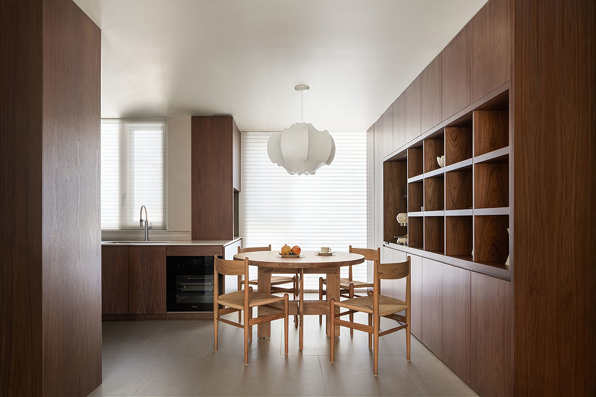 Modern residential kitchen featuring wooden furniture, a round dining table with chairs, and a large window with blinds.