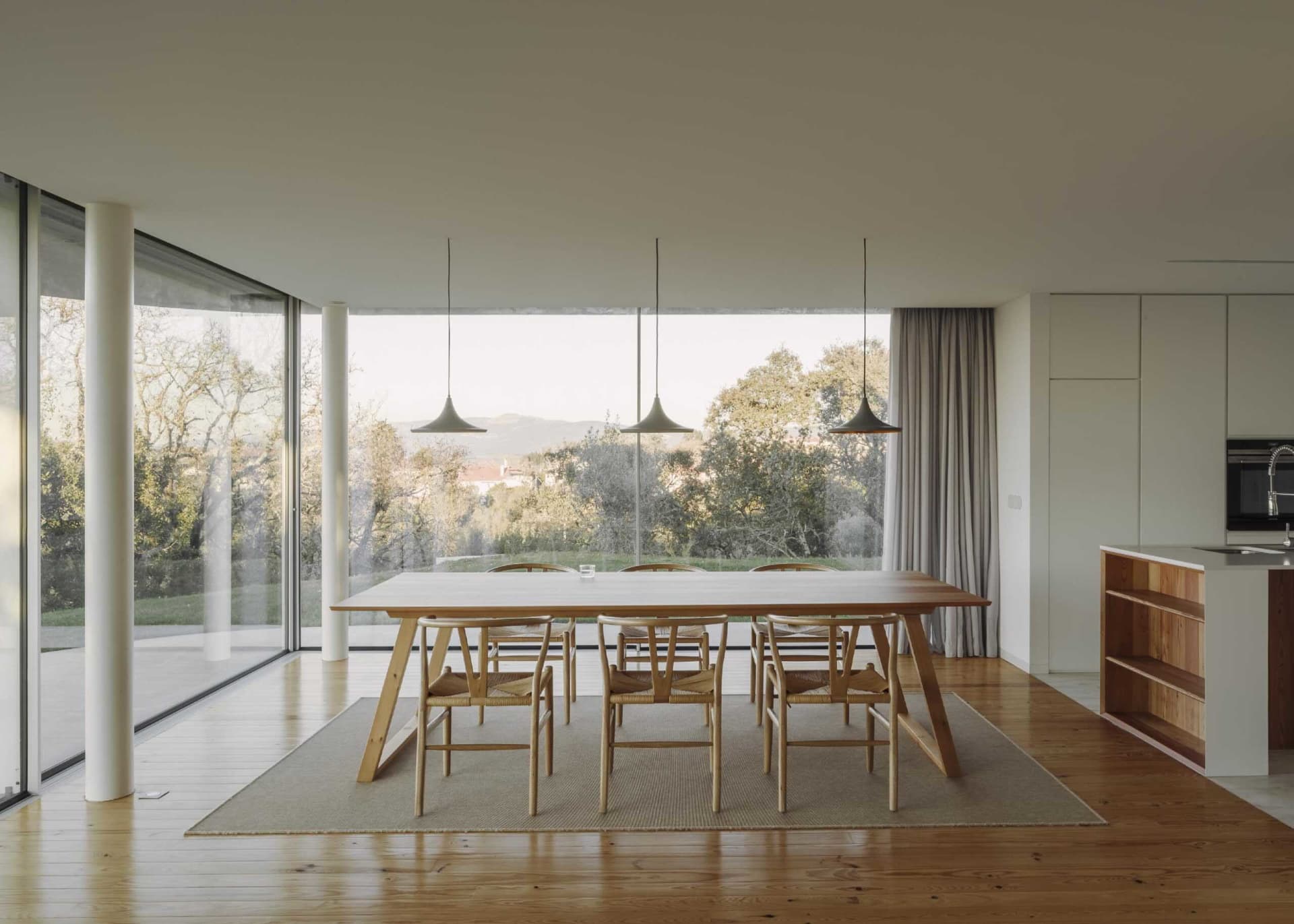 A modern living-dining room featuring a wooden dining table and chairs, with a large glass window showcasing a scenic outdoor