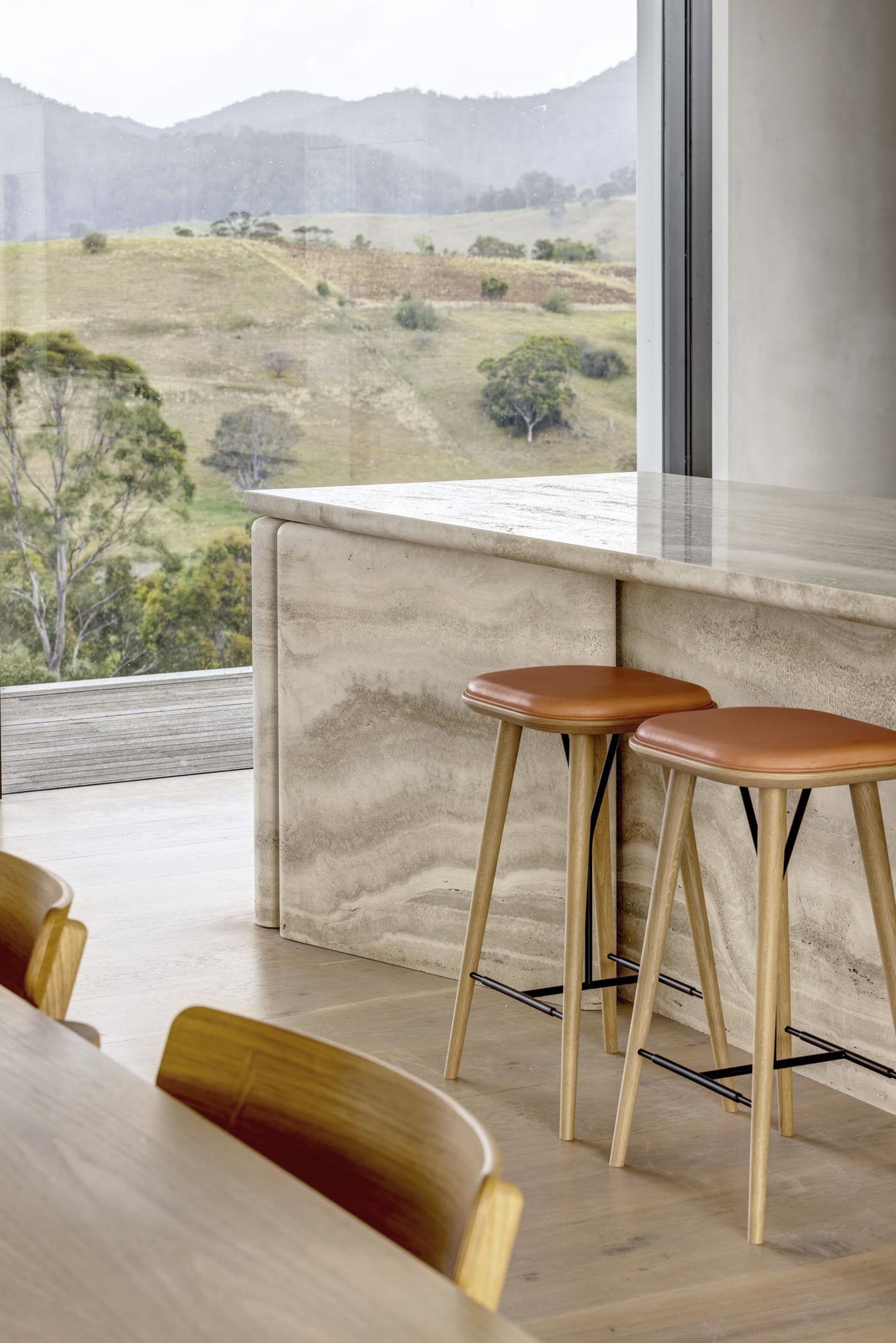 Modern kitchen with marble countertop and wooden stools overlooking a scenic landscape.