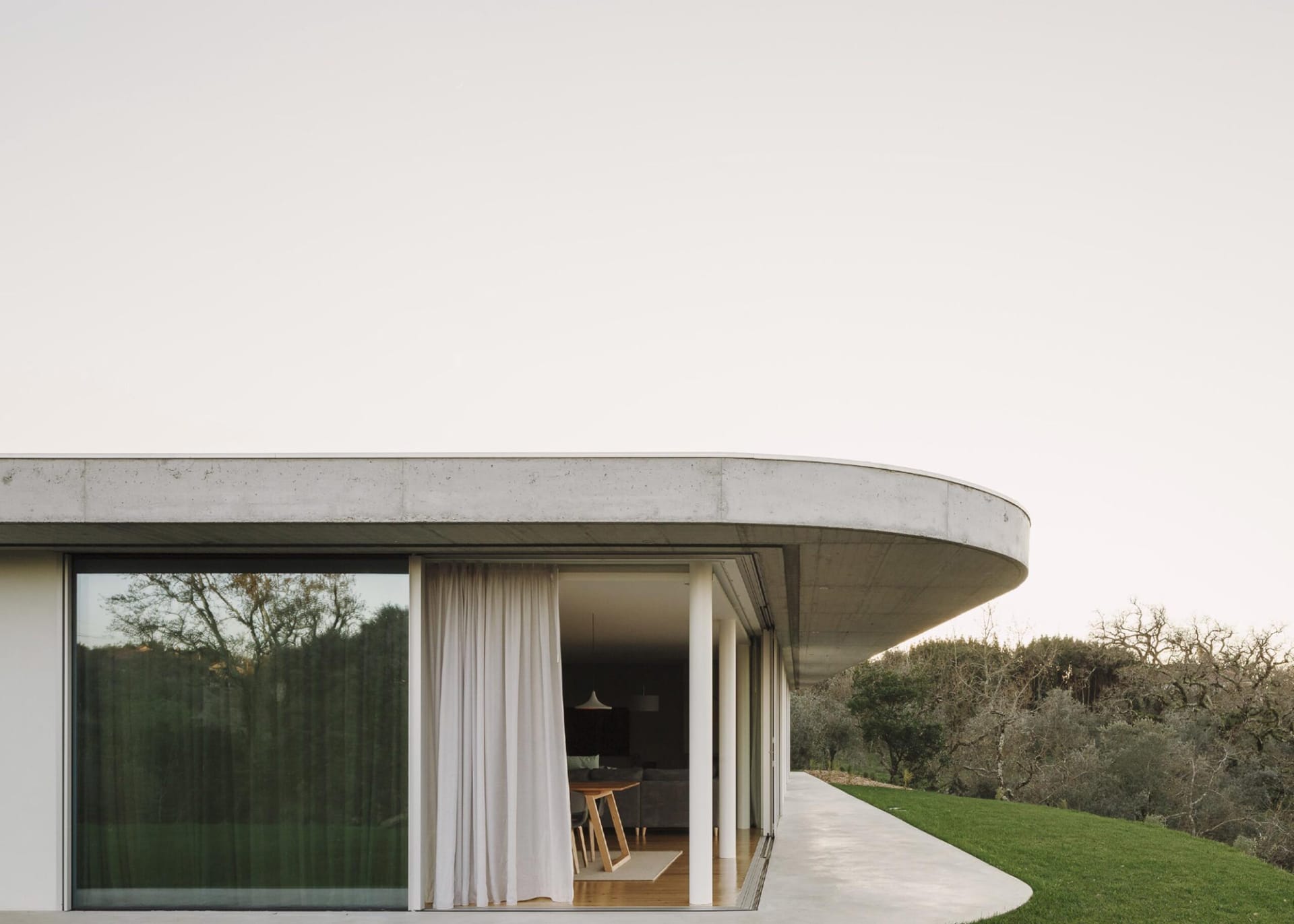 A modern minimalist house featuring a curved concrete roof and large glass windows.