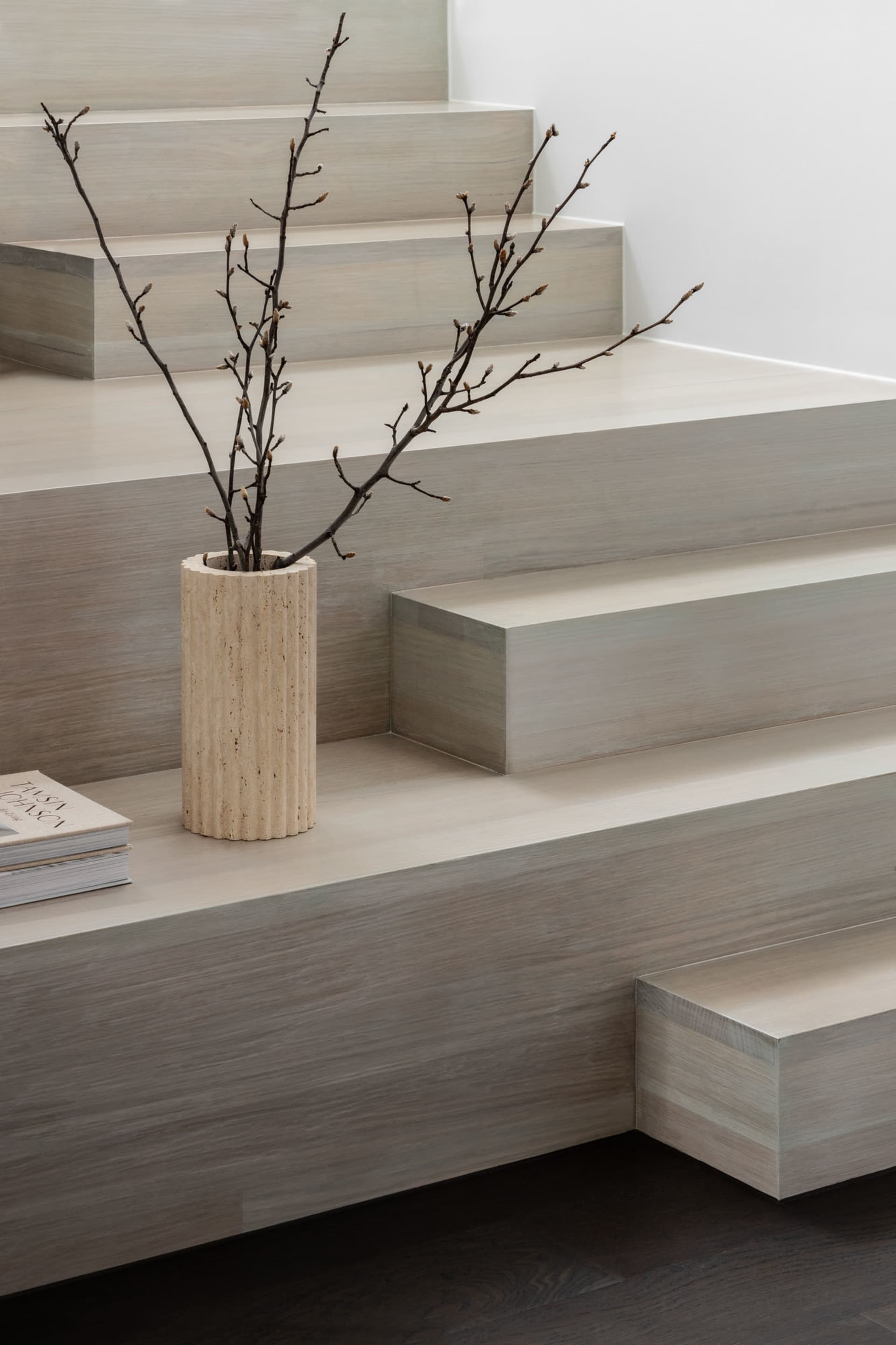 A minimalist interior featuring sleek, wooden stairs with a vase of twigs on the landing.