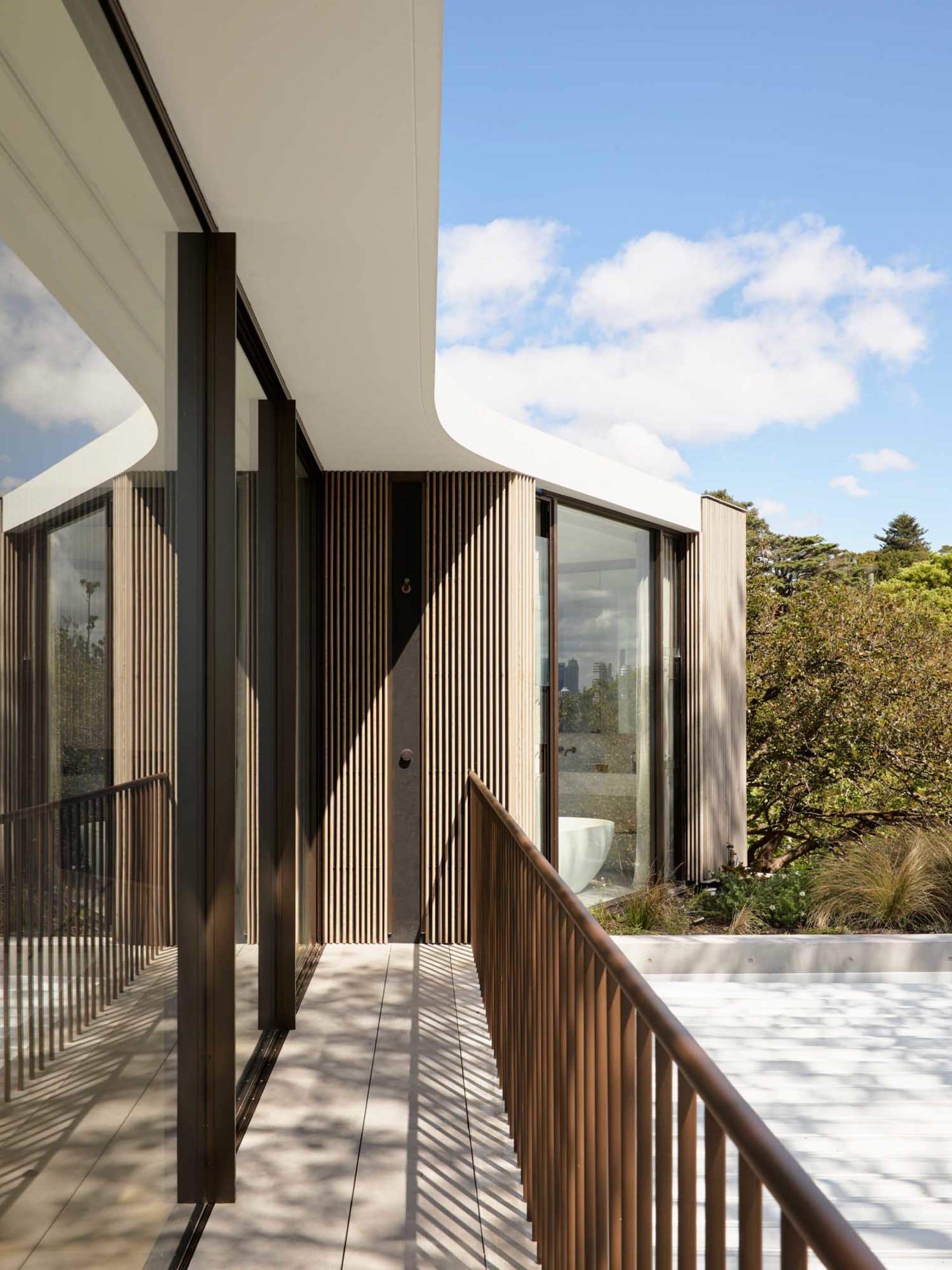 A modern residential exterior features a glass and wooden pool deck overlooking a bathroom interior.