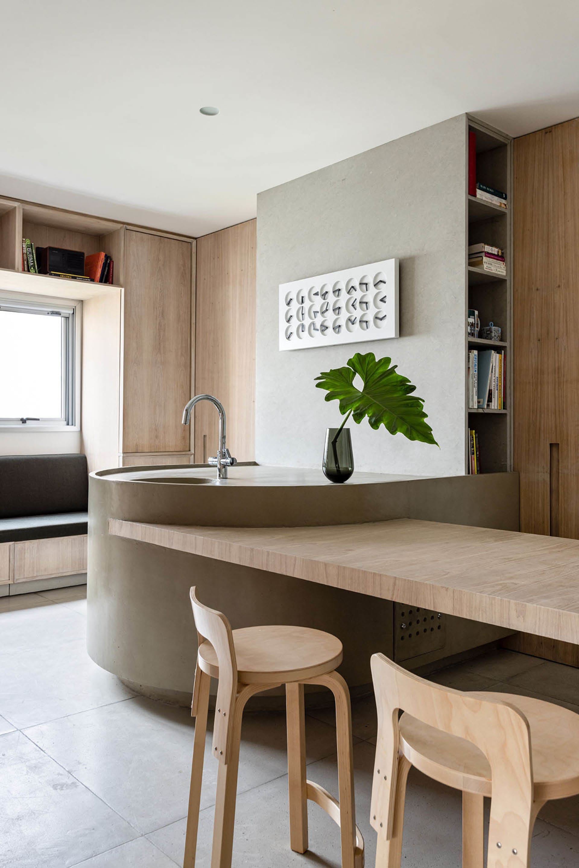 Modern kitchen with concrete countertop and sink, wooden stools, and green plant in a vase.