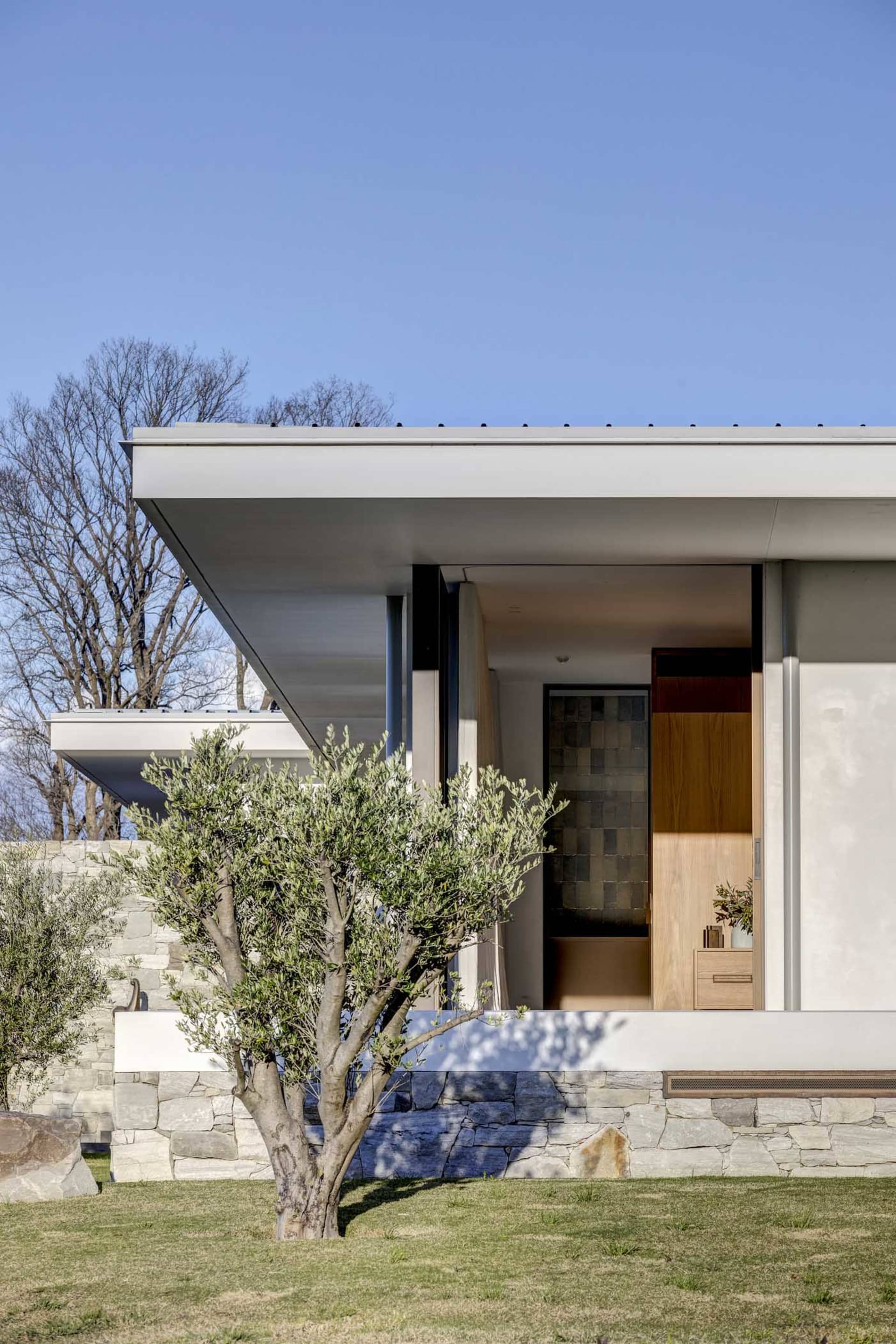 A modern residential exterior featuring stone walls, glass windows, and wooden elements.