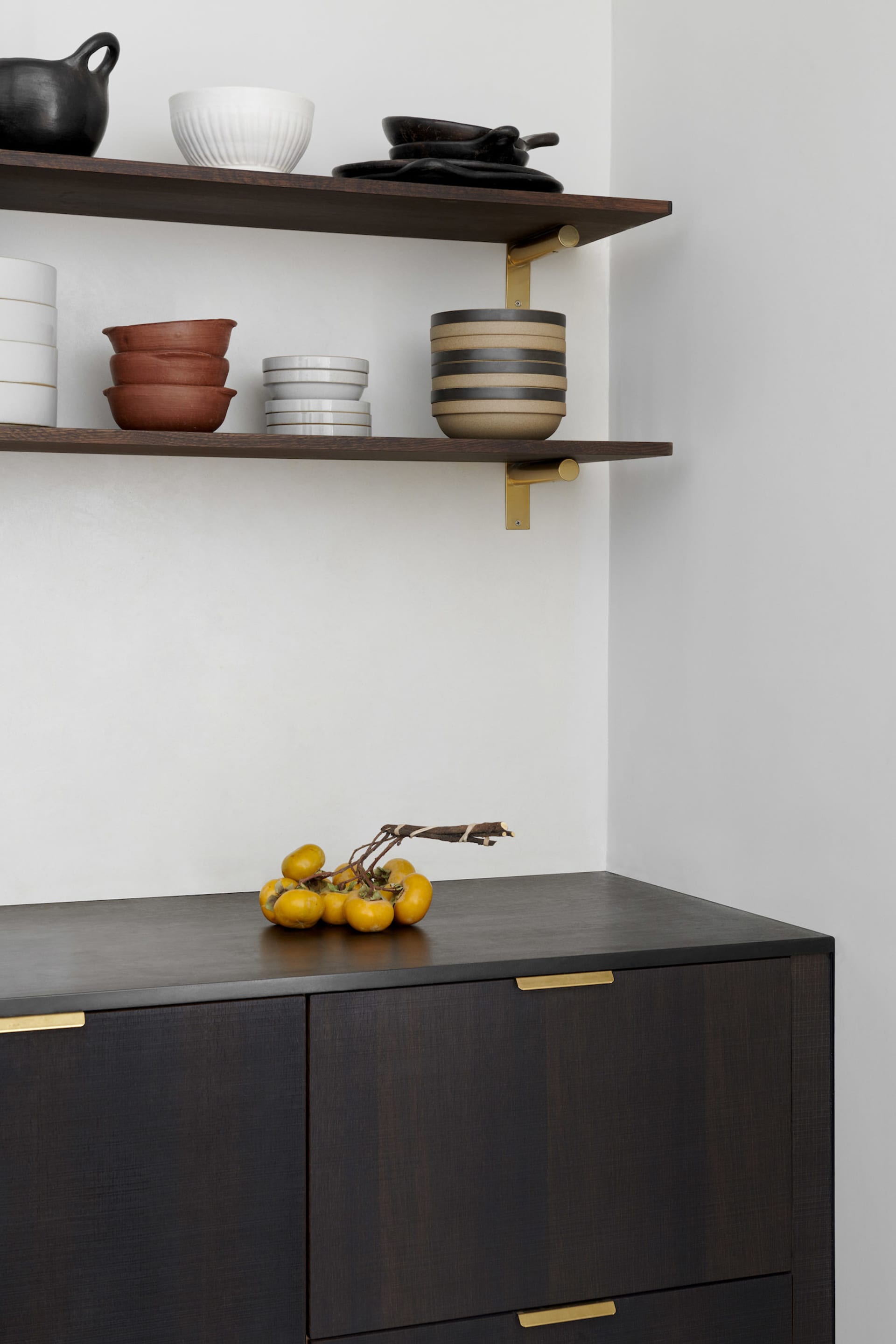Modern storage cabinet with wooden finish and brass accents containing bowls and other items.