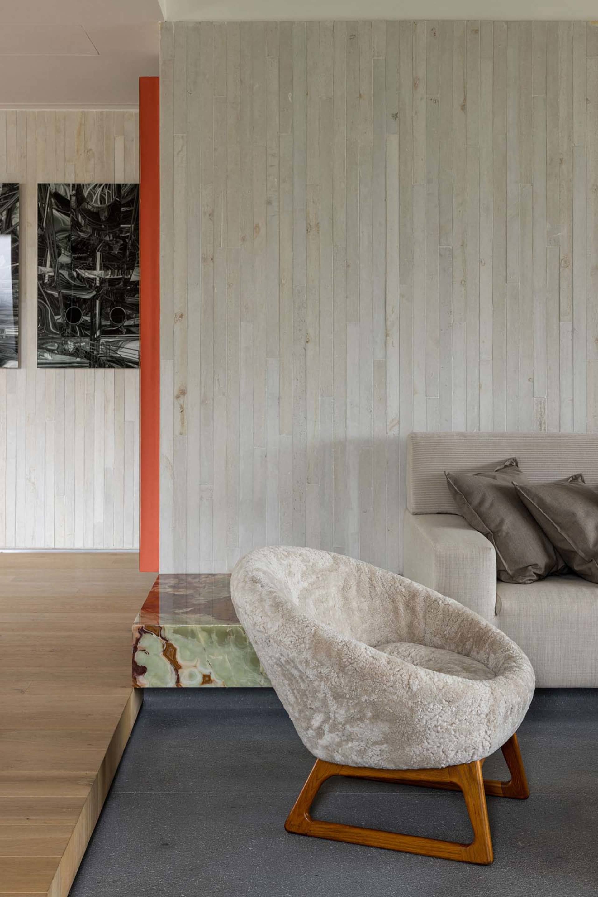 A modern living room with a concrete wall, wooden floors, a marble table, and upholstered seating.