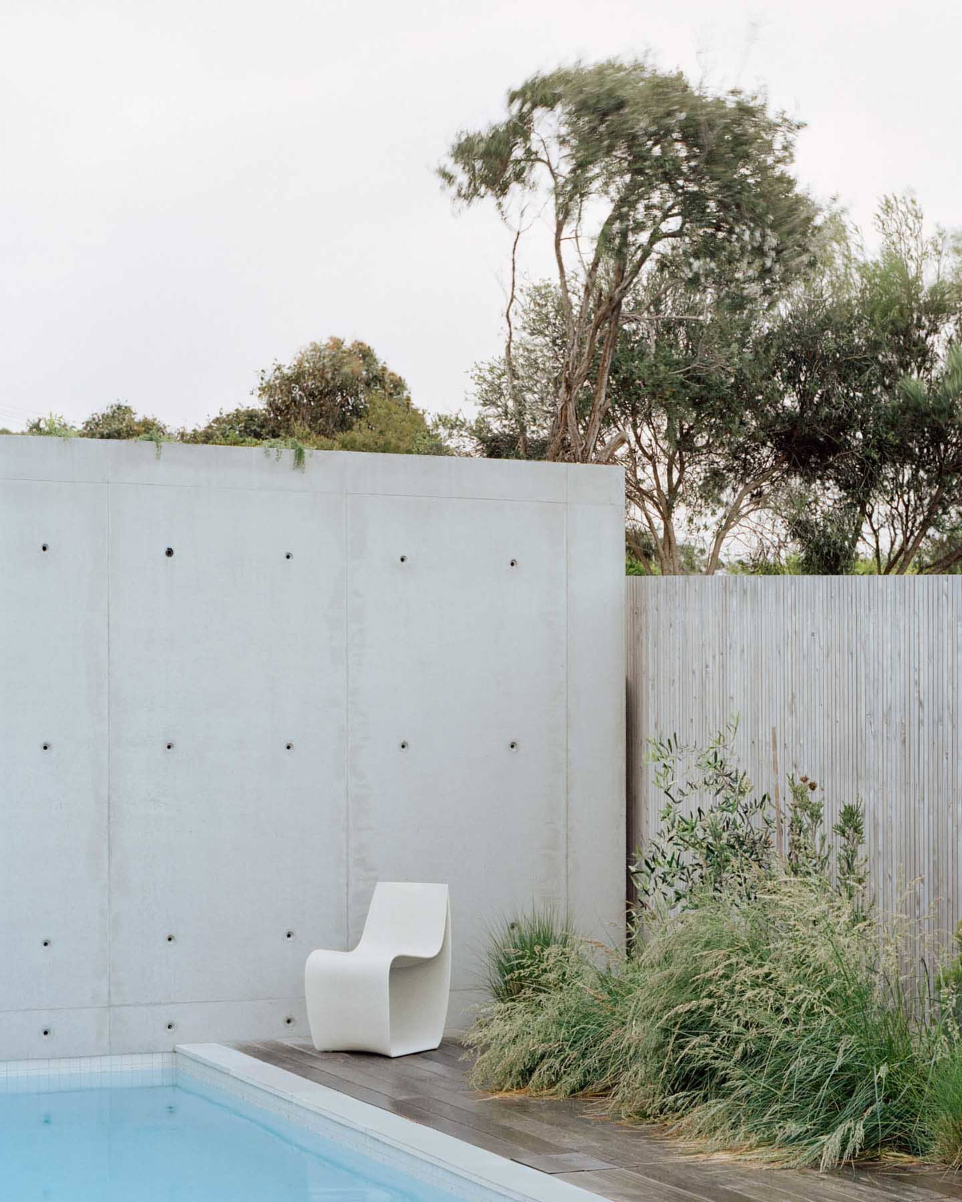 Modern interior with a concrete wall and white chair beside a pool.