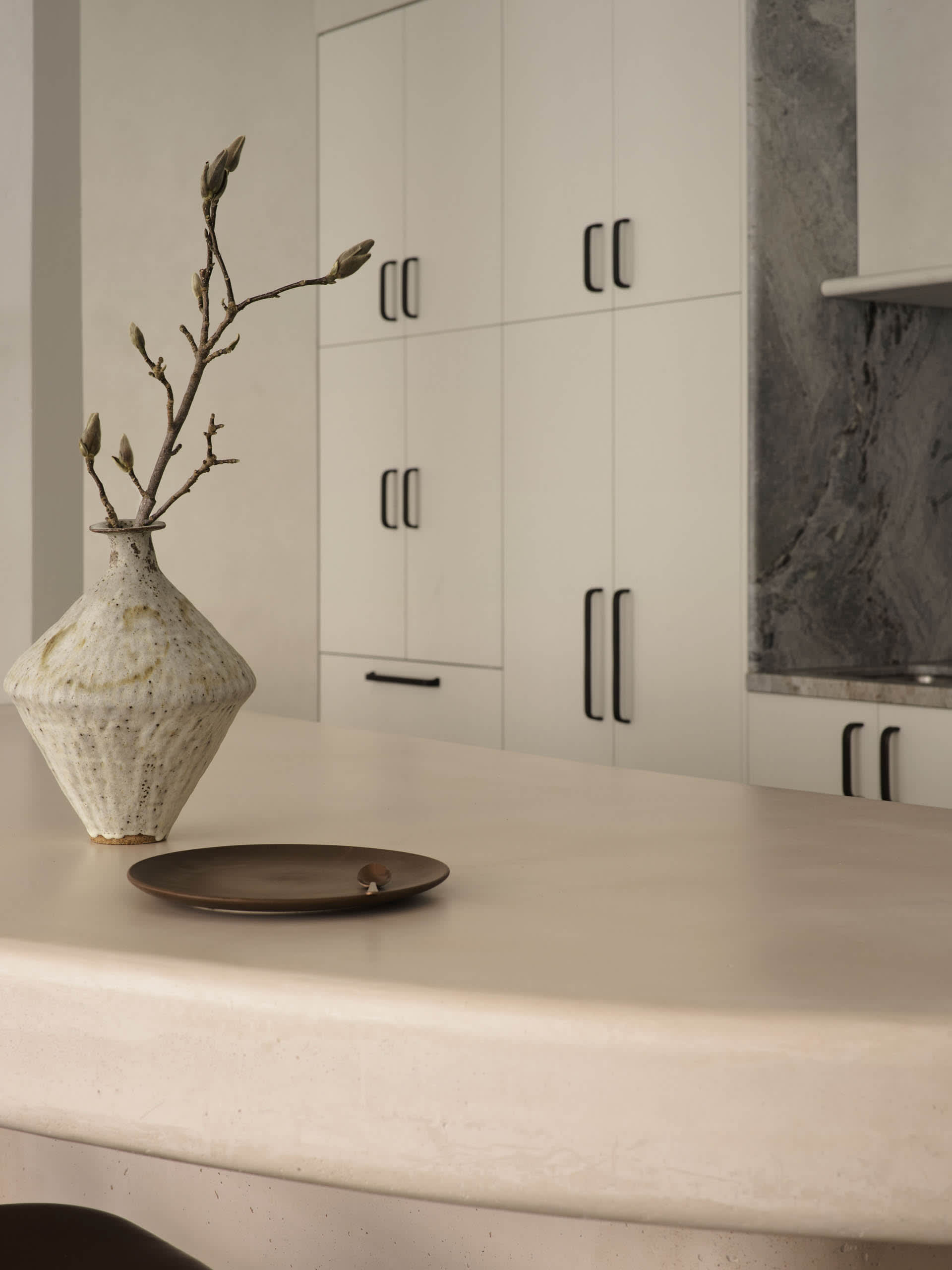 A modern kitchen features a concrete countertop with a minimalist vase and plate as decorative elements.