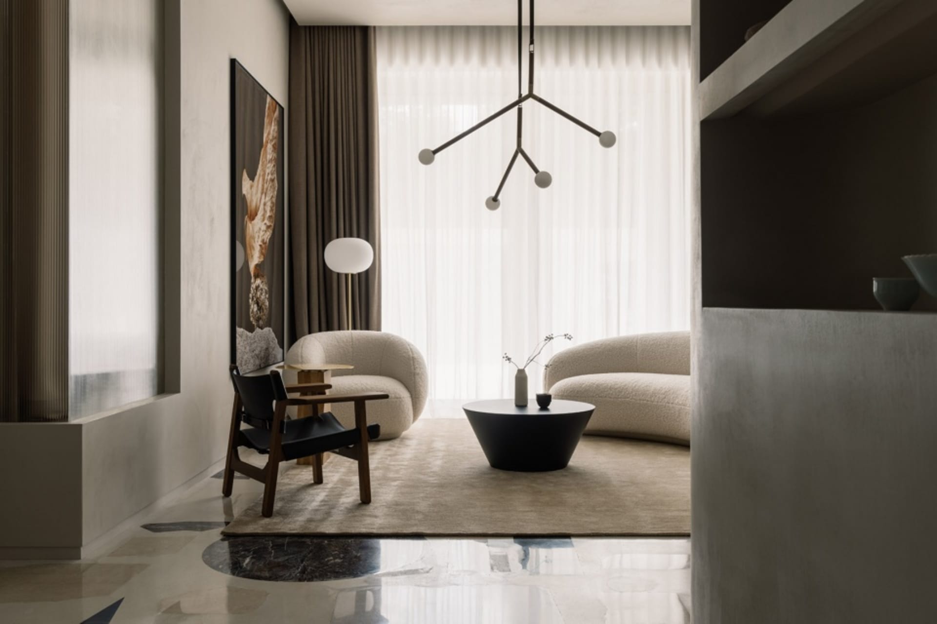 A modern living room with neutral-colored furniture, a round coffee table, and a minimalistic chandelier hanging above the se