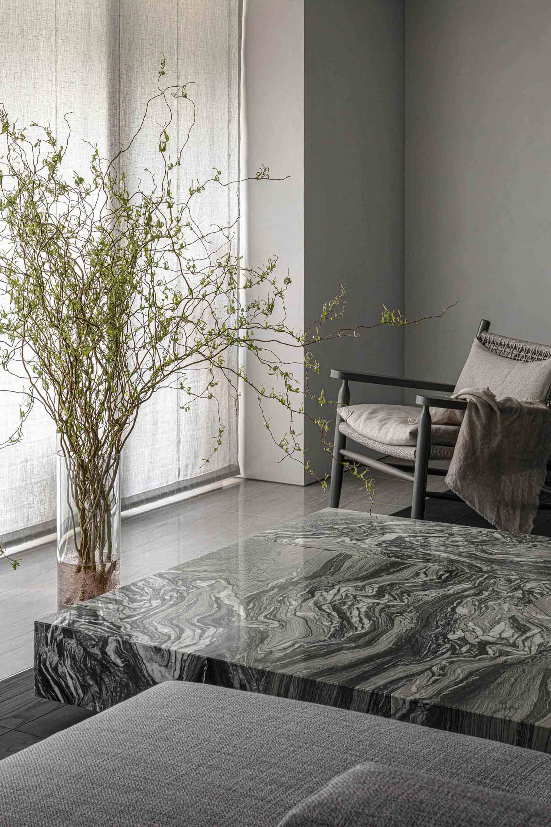 A modern living space featuring a sleek marble coffee table adorned with a vase of greenery and a comfortable upholstered cha