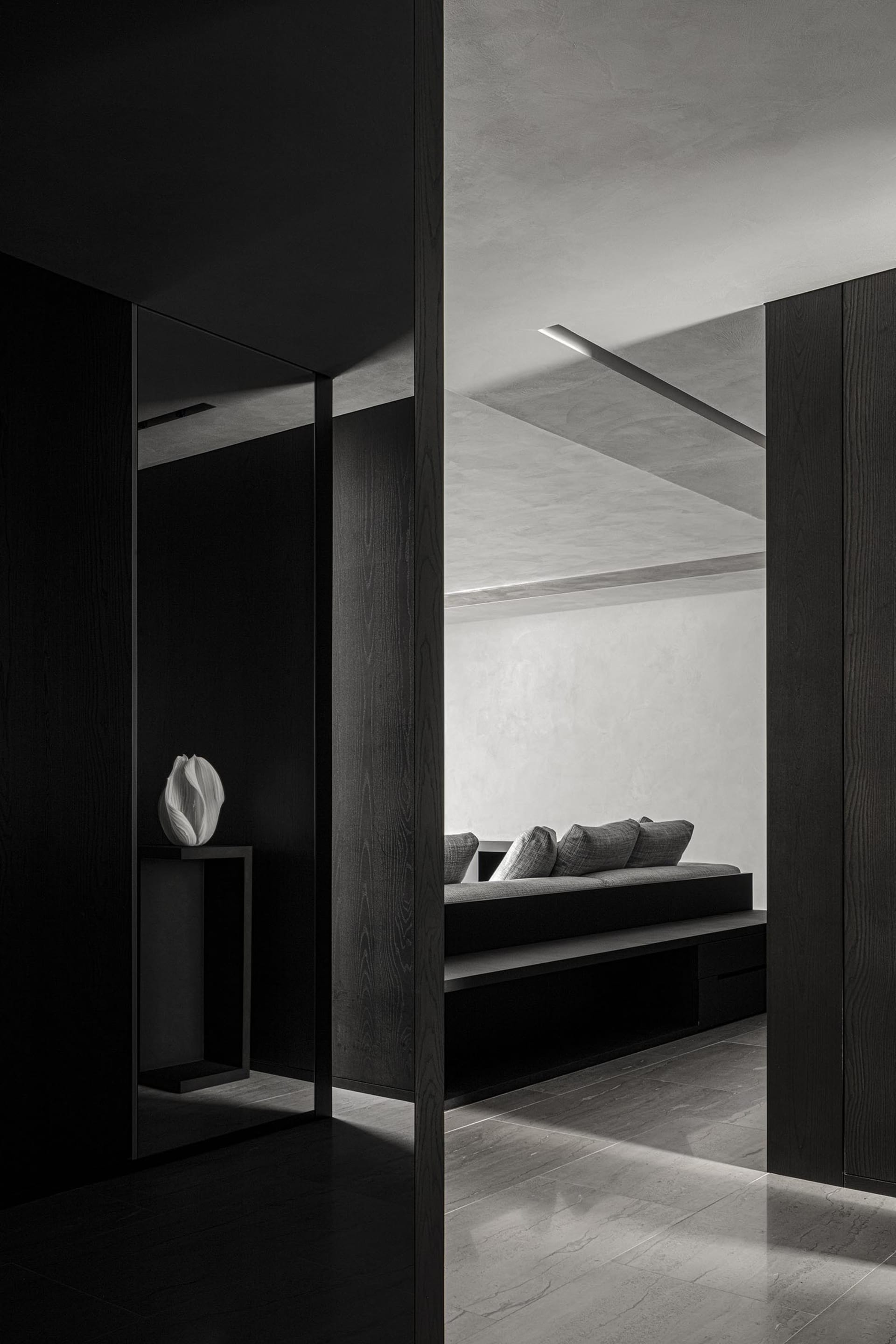 A modern minimalist living room with concrete walls, a built-in sofa, and a minimalist vase on a side table.