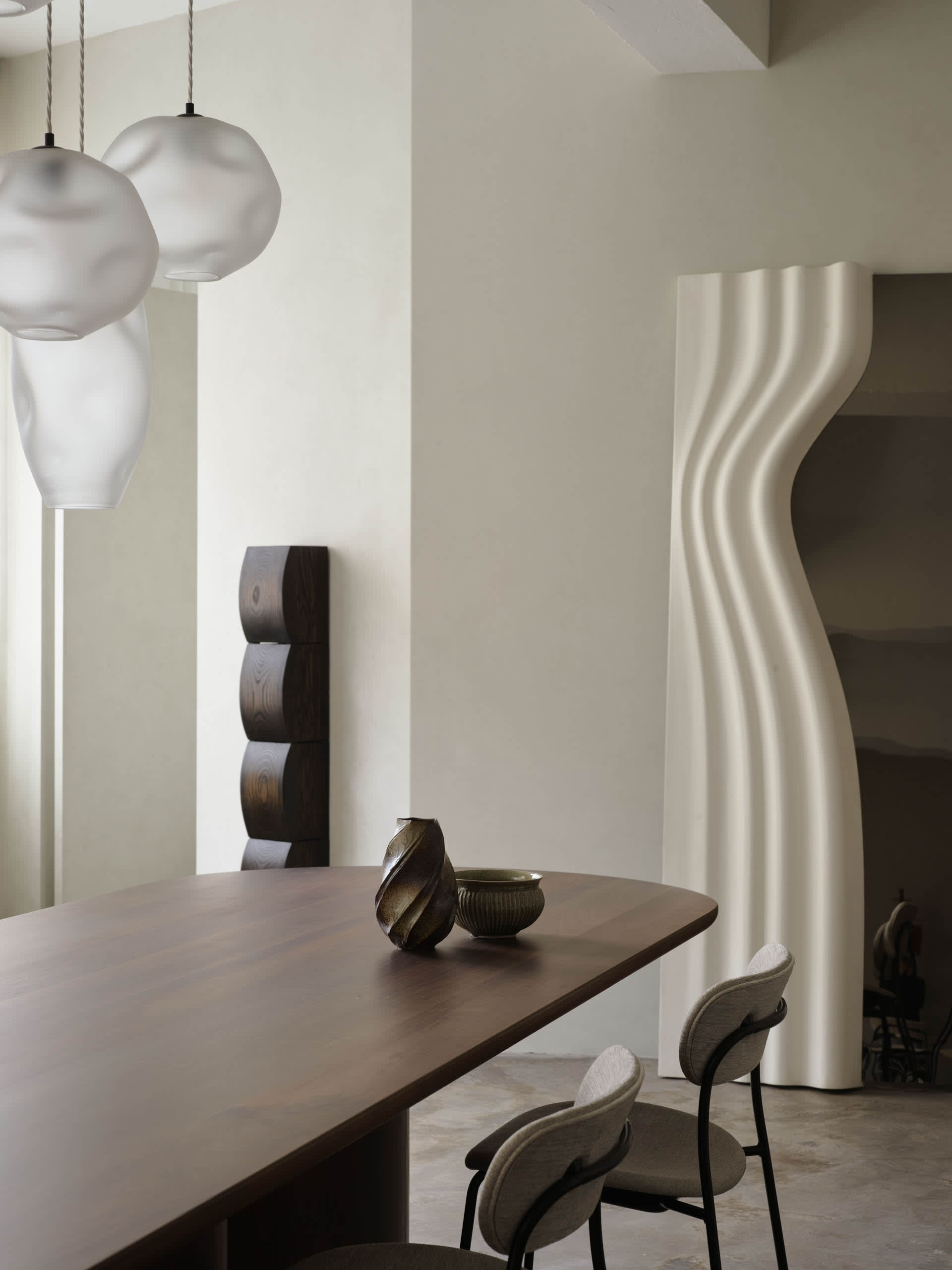 Modern minimalist dining room with a wooden table adorned with decorative vases and contemporary pendant lights.