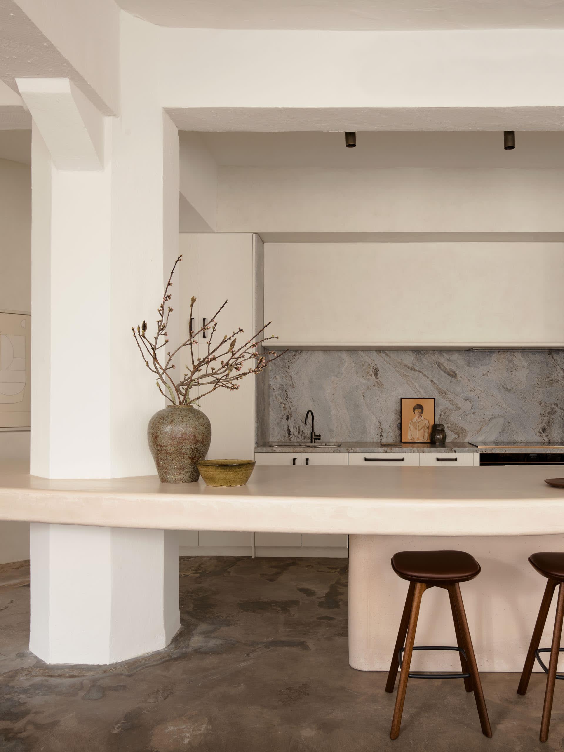 Modern minimalist kitchen with concrete accents and white cabinets, featuring a sleek countertop and minimalist decor.