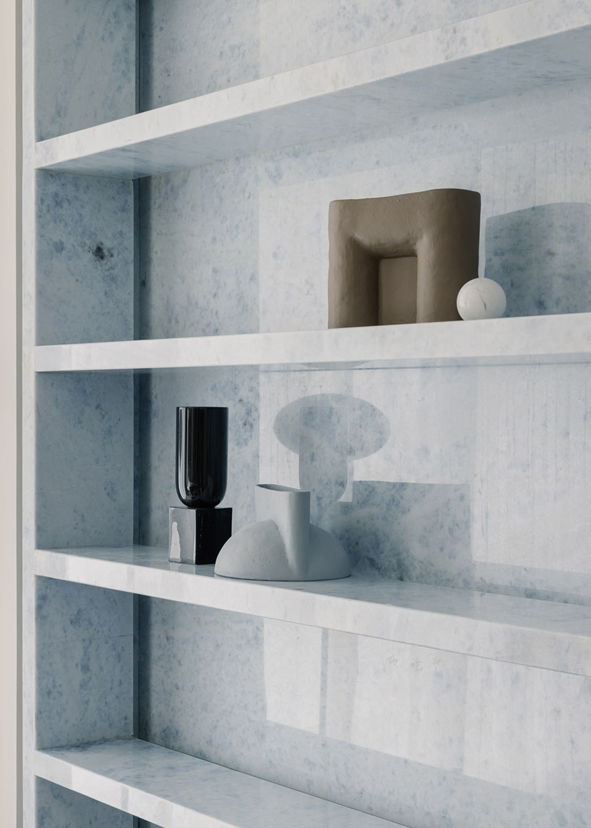 Minimalist marble shelving displaying modern abstract sculptures and vases.