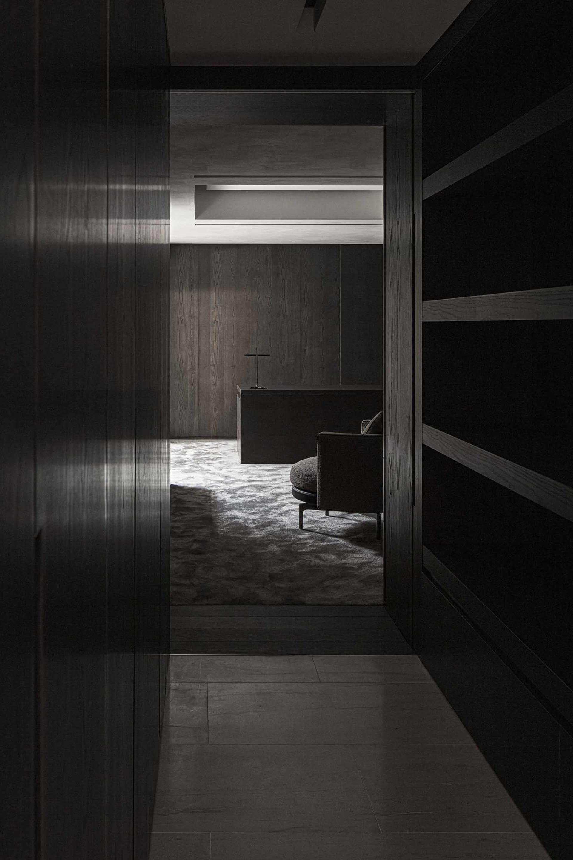 Modern black living room with minimalist furniture and dark wood walls and cabinets.