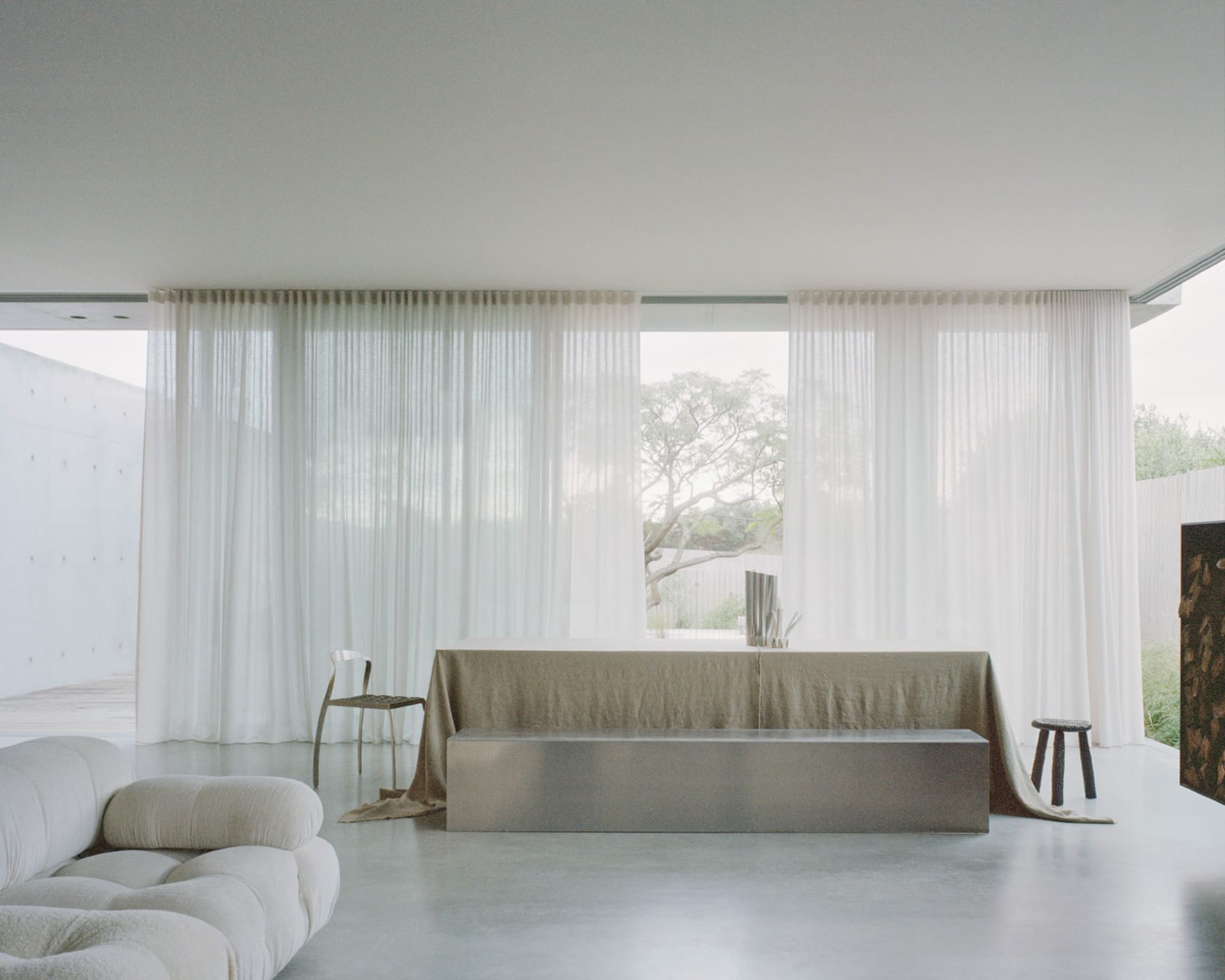 A modern living room with large windows, glass curtains, and concrete furniture.