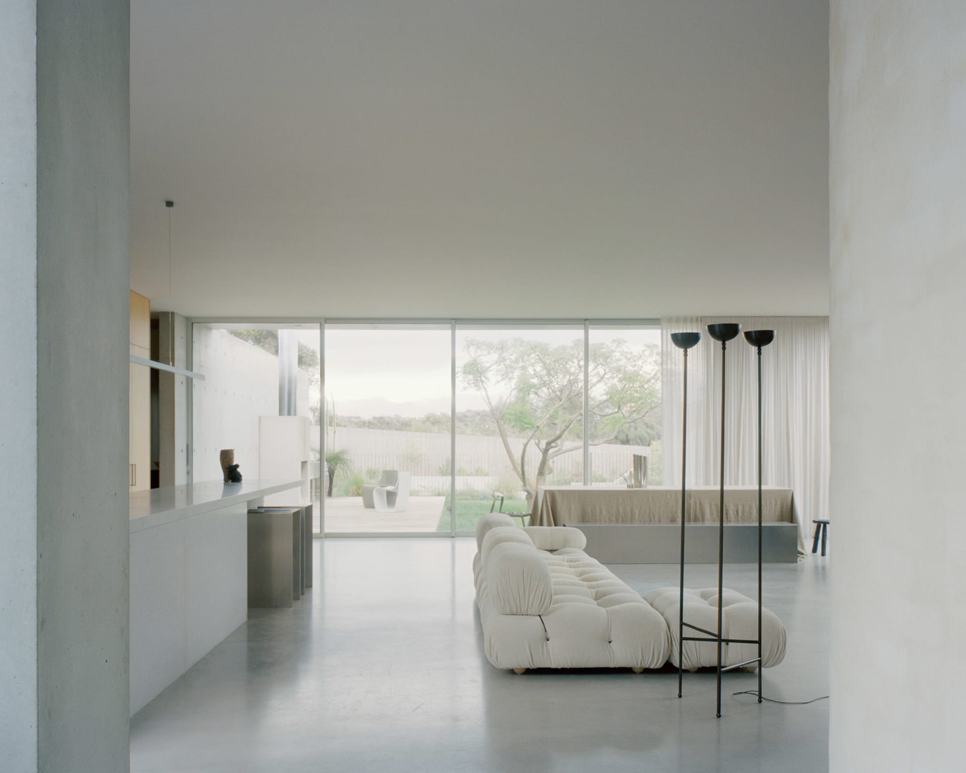 Modern minimalist living room with a white sofa, floor-to-ceiling windows, and a concrete floor.