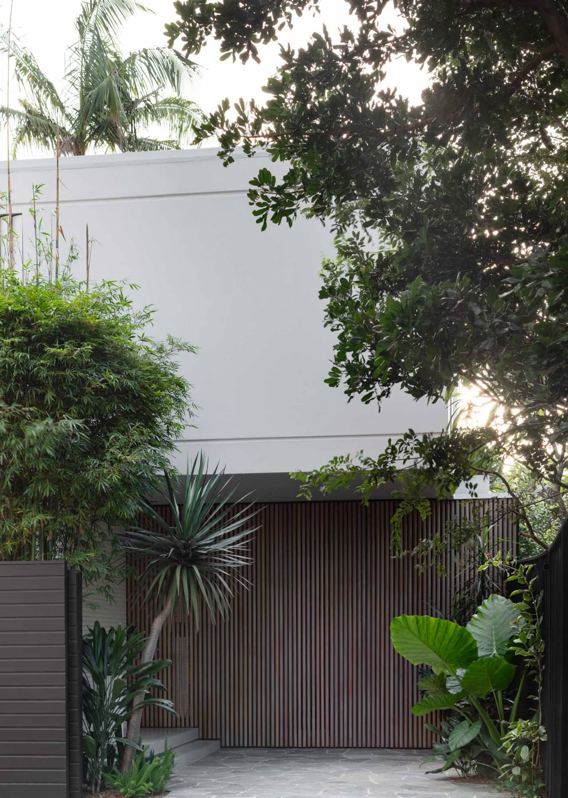 Modern private residence exterior featuring a wooden Sliding Gate with lush greenery surrounding it.