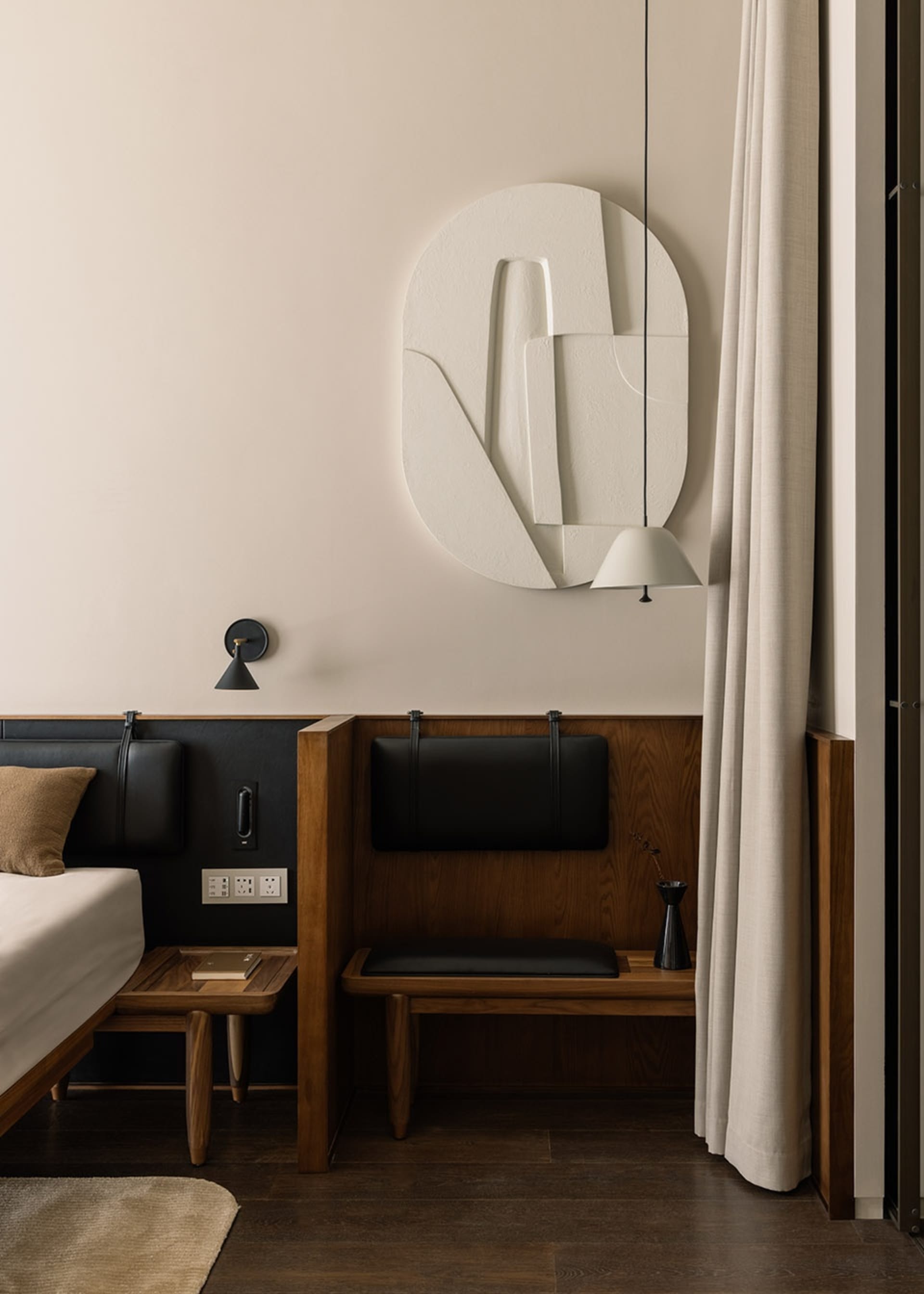A modern bedroom with wooden furniture, a white relief sculpture on the wall, and a hanging lamp.