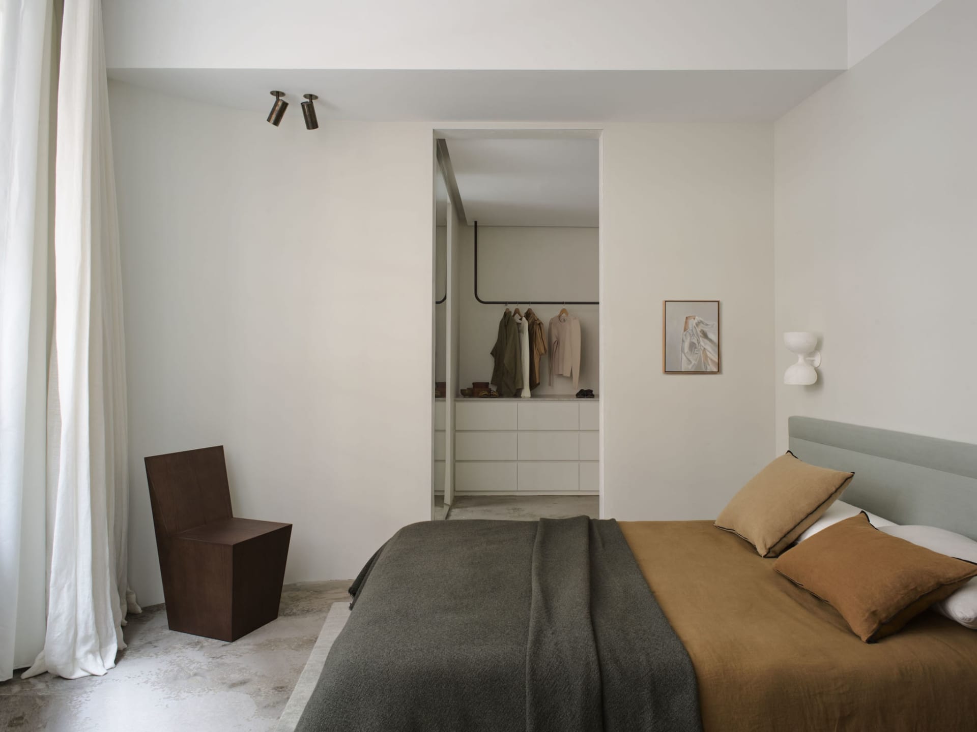 A minimalist bedroom featuring a minimalist wooden chair, concrete flooring, a bed with fabric bedding, and an open closet wi
