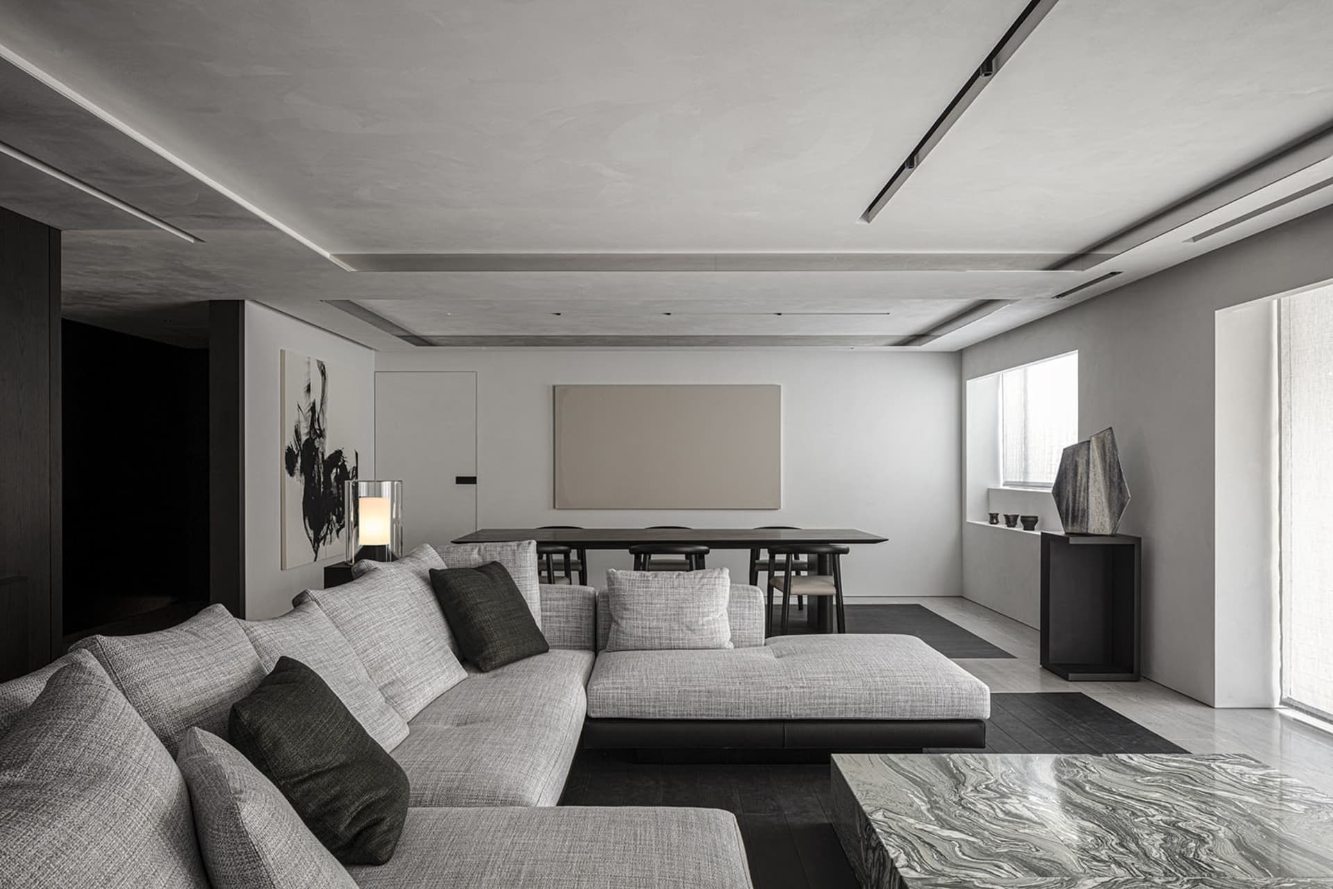 A modern living room with concrete walls and floor, featuring a gray sectional sofa and a black marble coffee table.