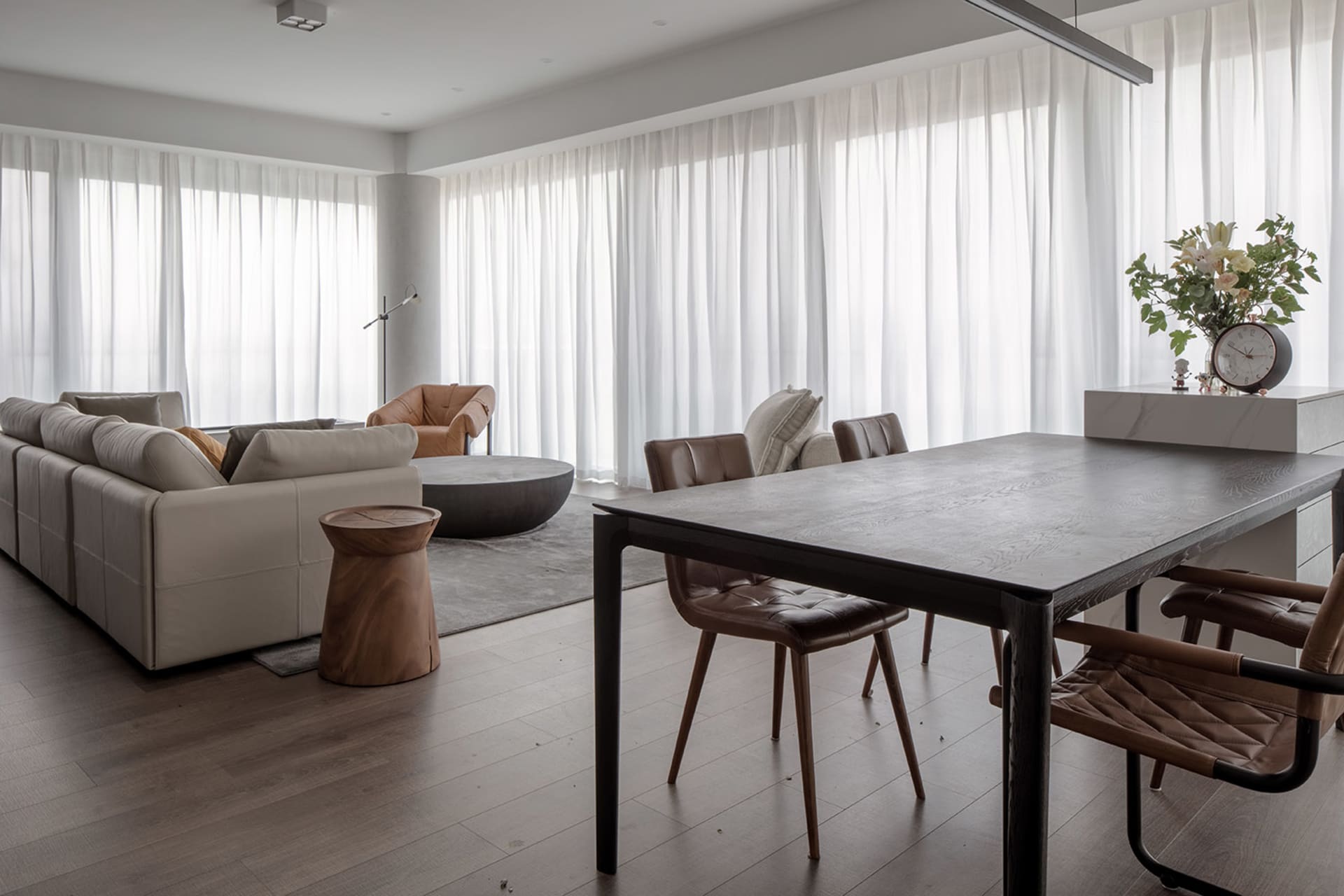 Modern industrial living room with wooden furniture and leather accents, featuring a large sofa, chairs, and a dining table.