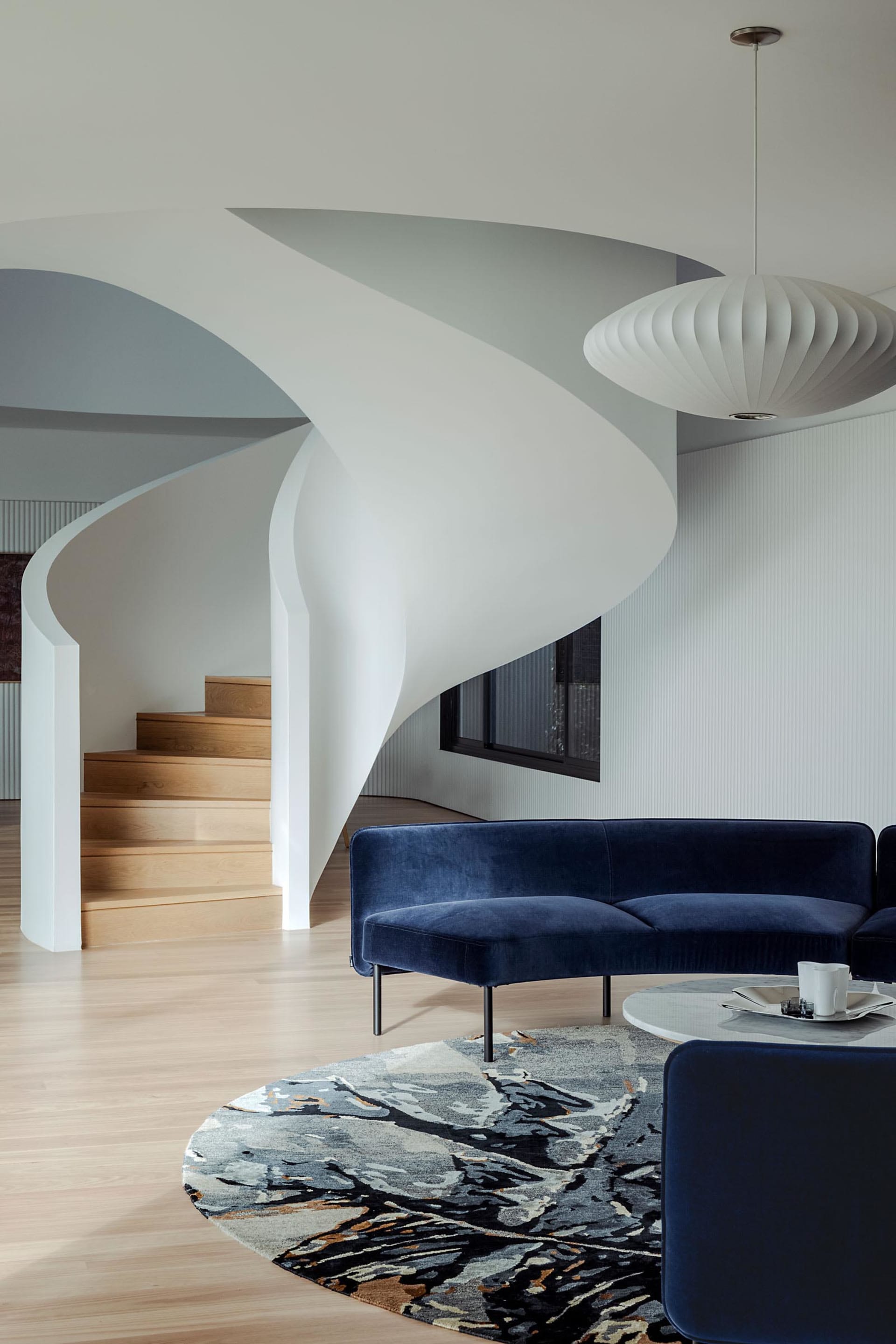 A modern living room featuring a navy blue velvet couch, a round coffee table, and a spiral staircase.