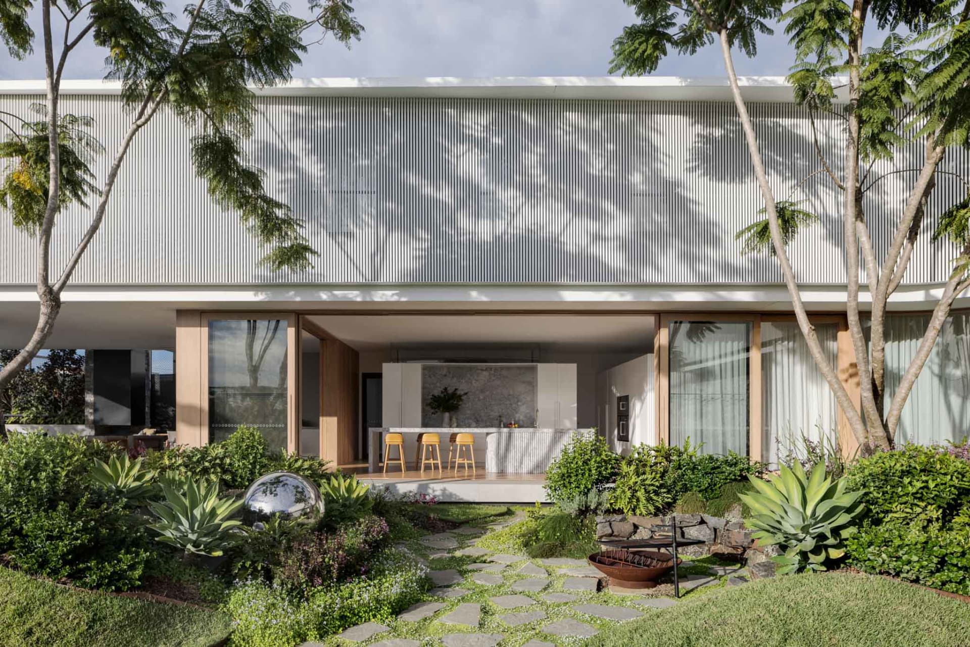 A modern residential exterior featuring a metal-clad facade with large windows and a landscaped garden.