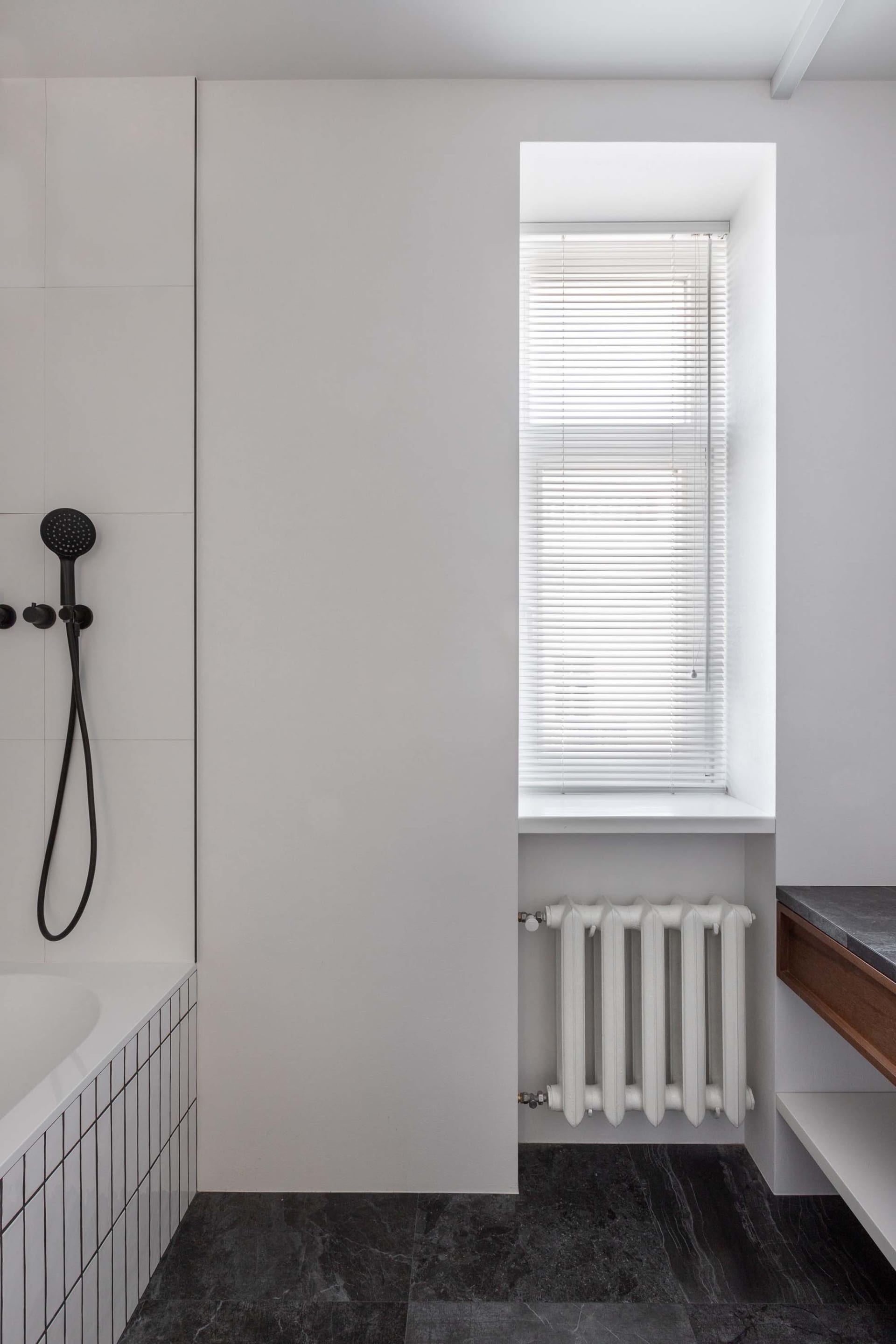 A modern minimalist bathroom with concrete elements, a window with blinds, and a radiator below it.