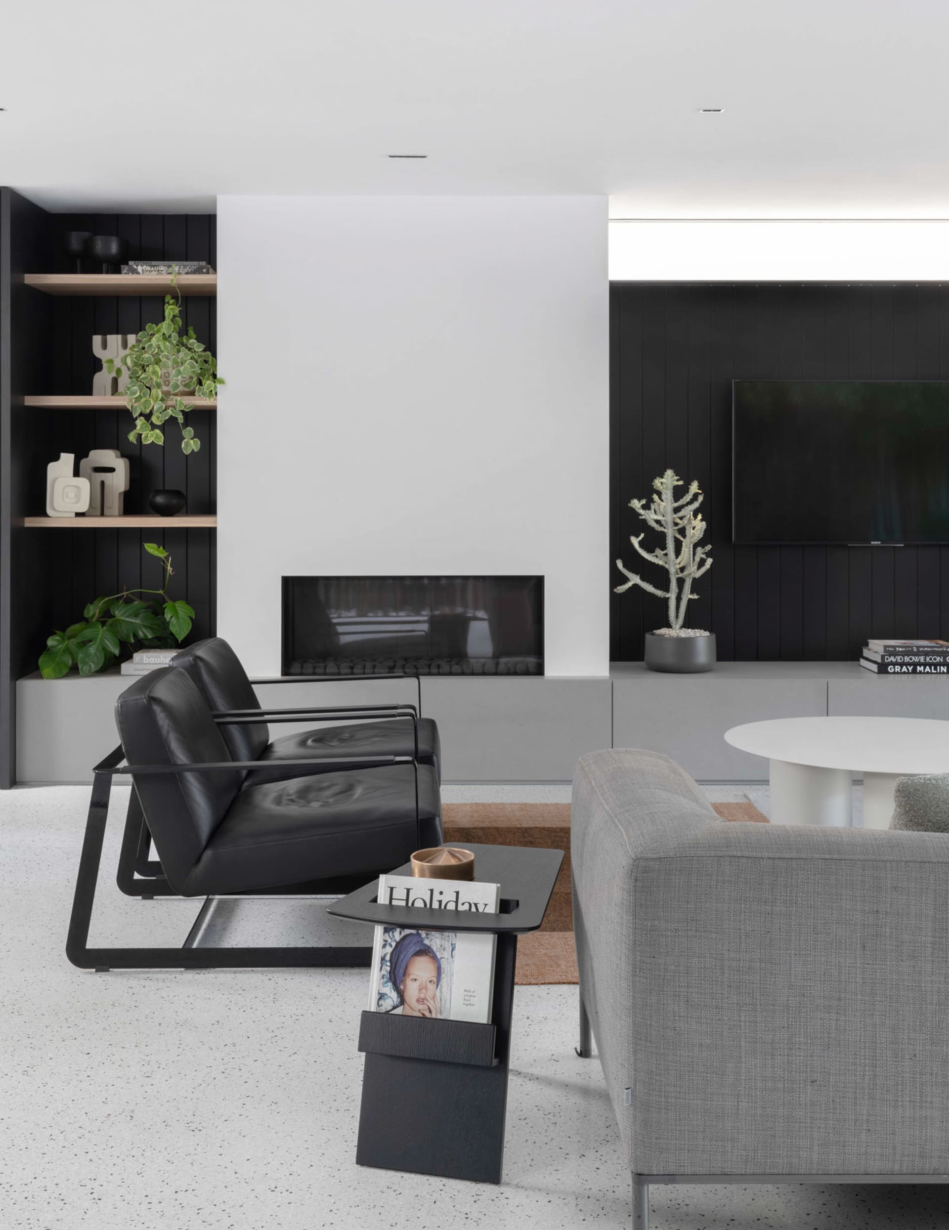 Minimalist living room furnished with black metal armchair and gray fabric sofa, featuring a modern fireplace, black shelving