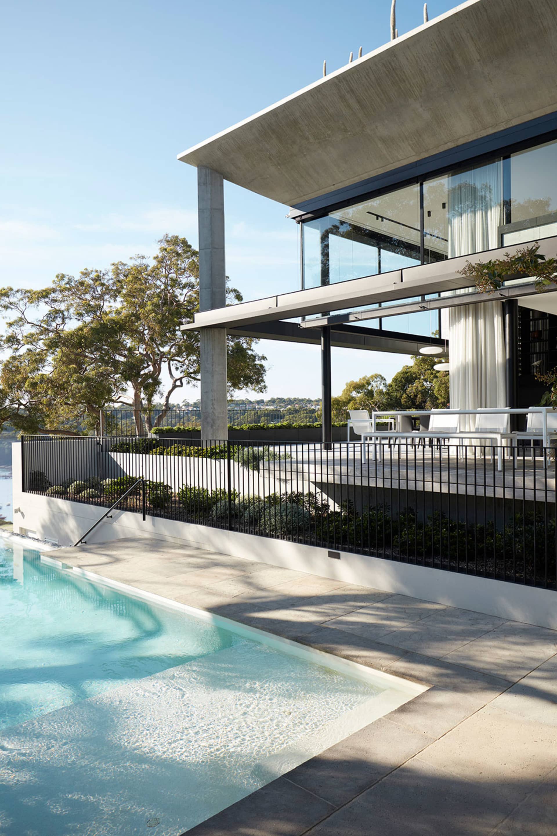 A modern residential exterior designed with concrete and glass materials, featuring a swimming pool and a spacious balcony ov