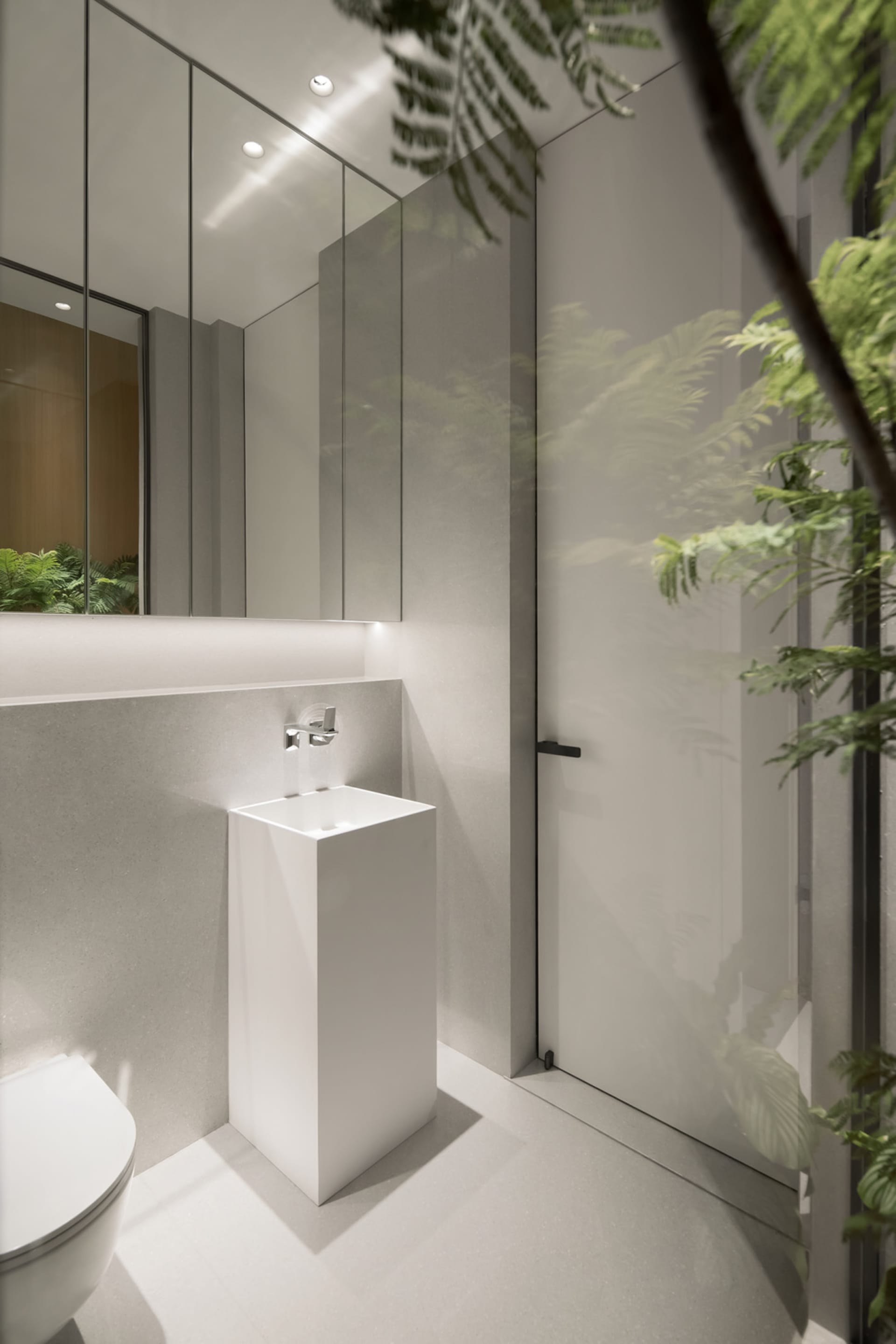 A modern minimalist bathroom with a concrete floor, minimalist white furniture, and a large mirror.