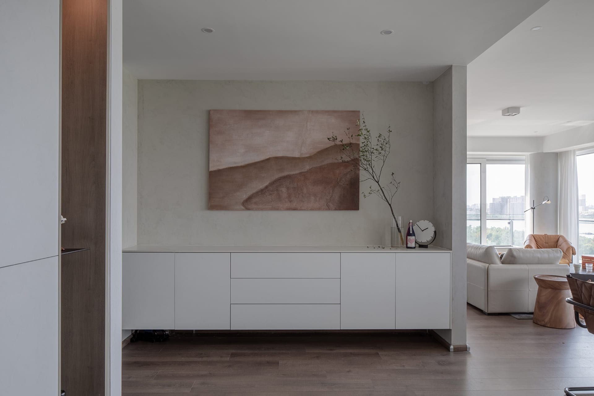 A modern living room with white furniture and a plant in a vase on a sideboard.