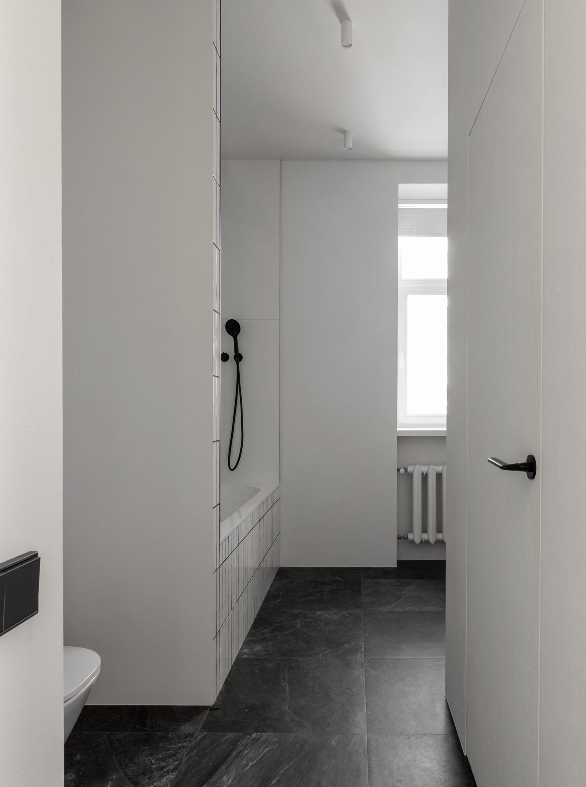 Modern minimalist white bathroom with black marble flooring and white tiled shower area.