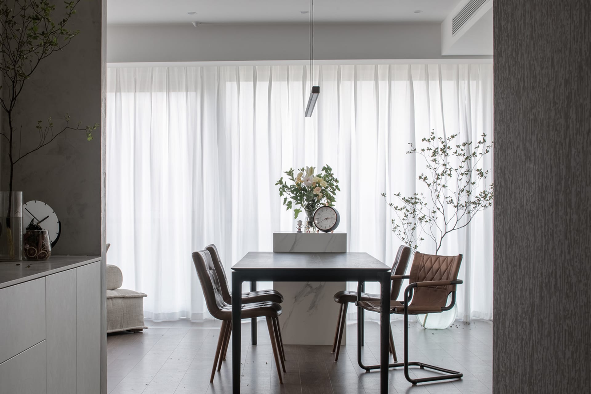 Modern minimalist dining room with white curtains, marble table, leather chairs, and indoor plants.