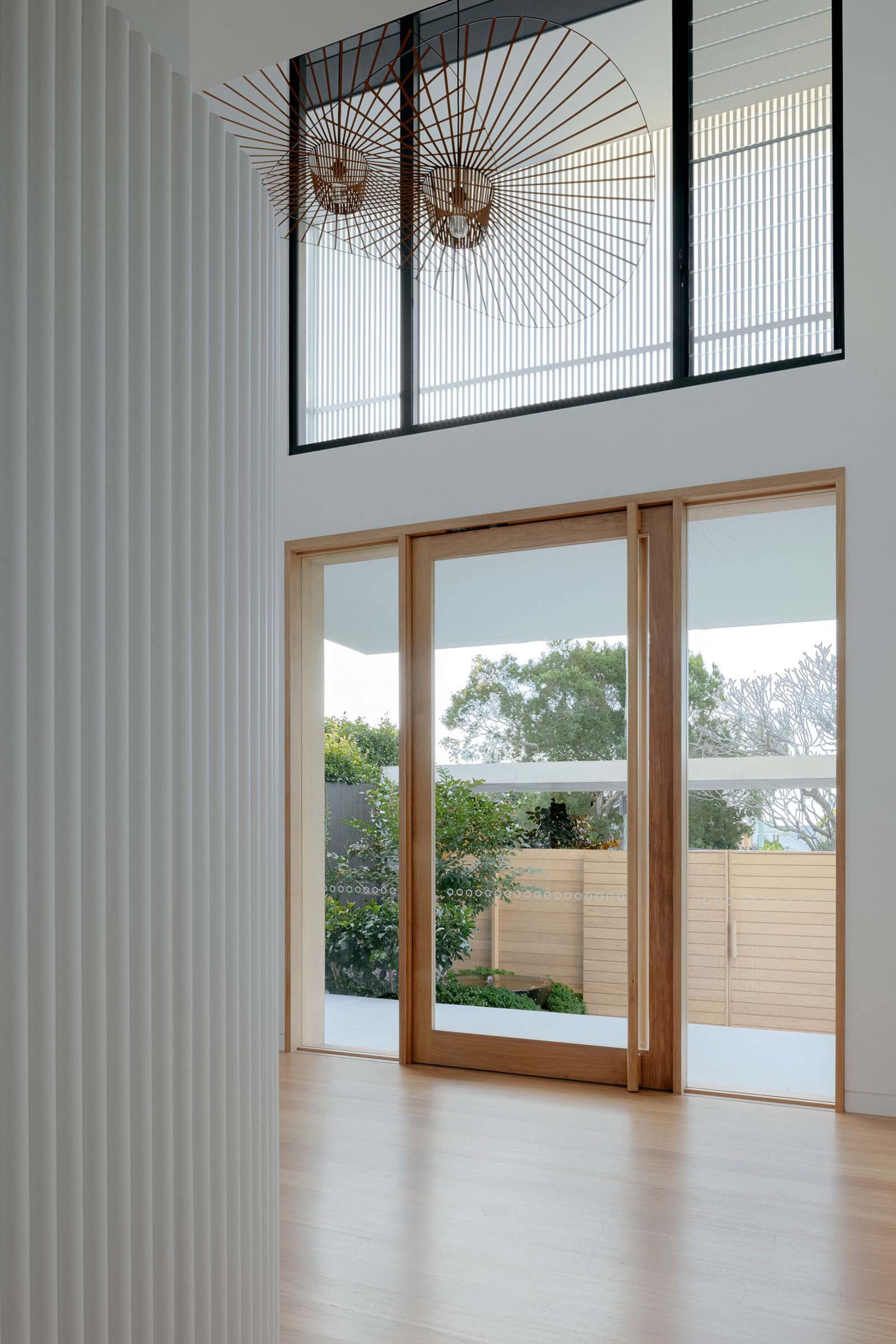 A minimalist living space featuring light-colored wood and glass doors, with a view of a green garden.